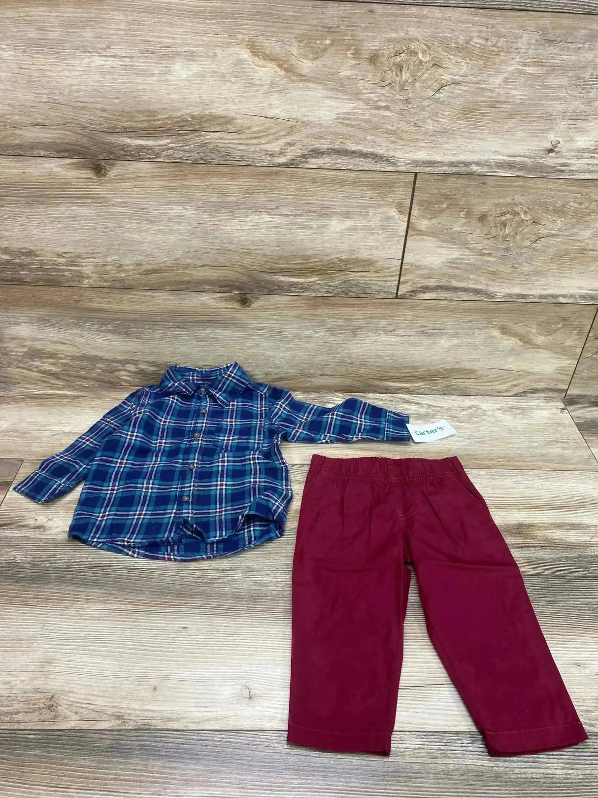 Flat lay of Carter’s 2-piece baby set: blue plaid long-sleeve button-up shirt and red elastic-waist pants on wood background, size 12 months