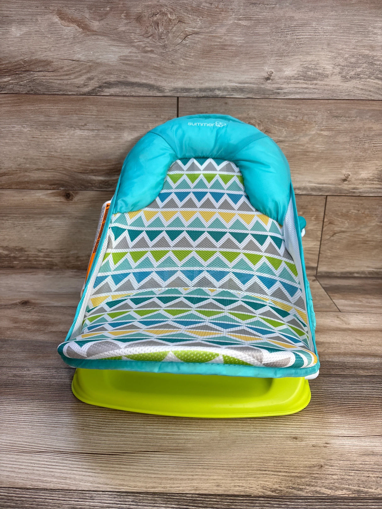 Colorful baby bath seat with geometric pattern, turquoise and green, on wood floor