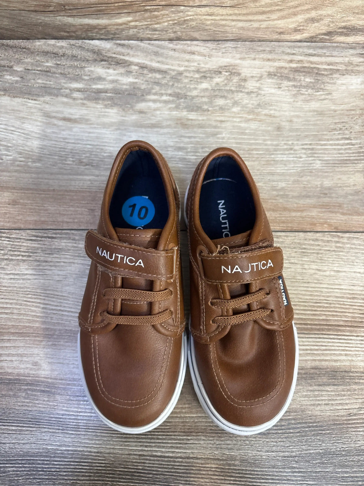 Top view of Nautica Calloway faux leather brown sneakers showcasing hook-and-loop straps and white soles on a wood-grain surface
