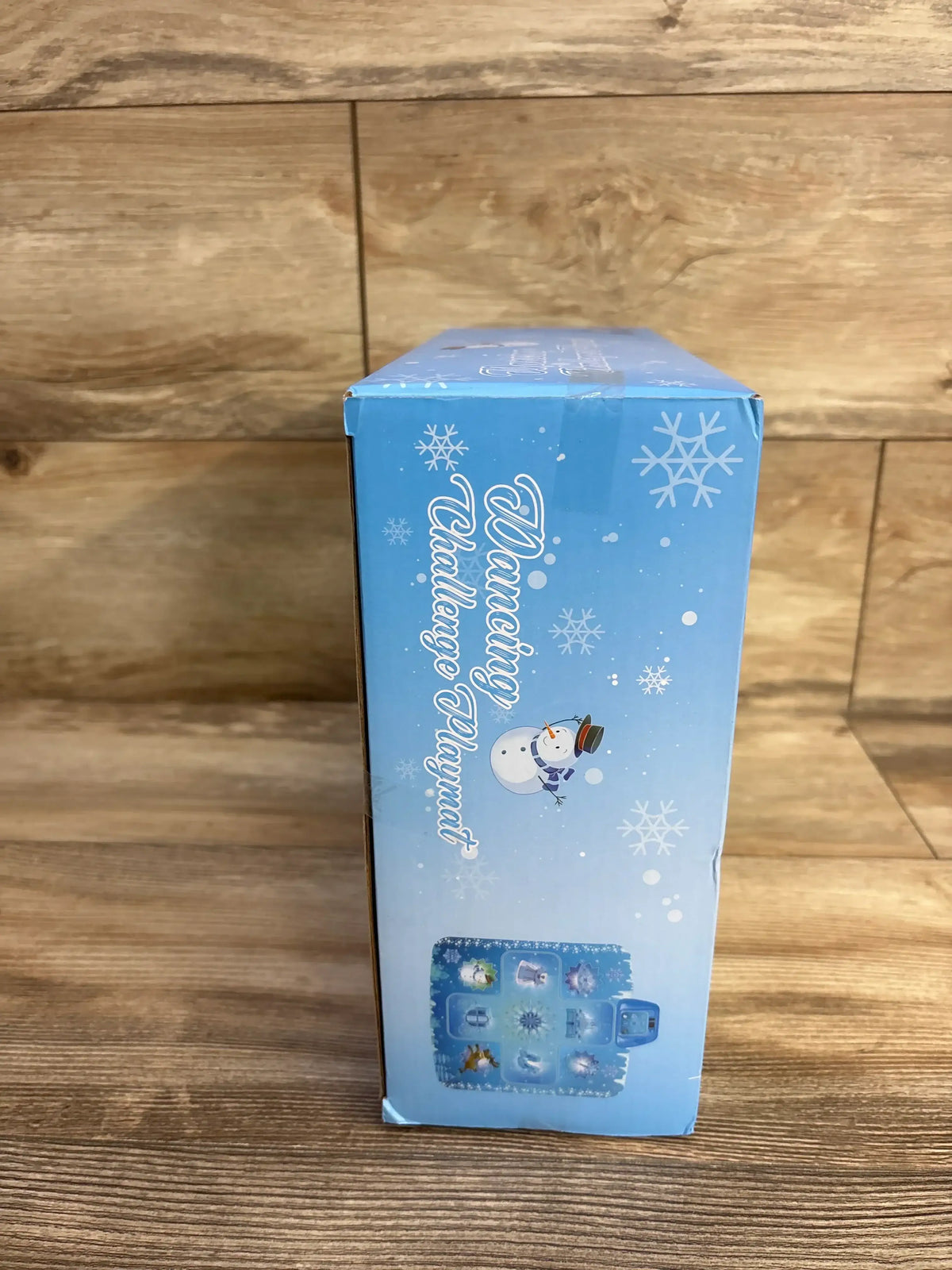 Side view of boxed GirlsHome Frozen electronic dance mat showing snowman graphic and product icon grid on wooden surface