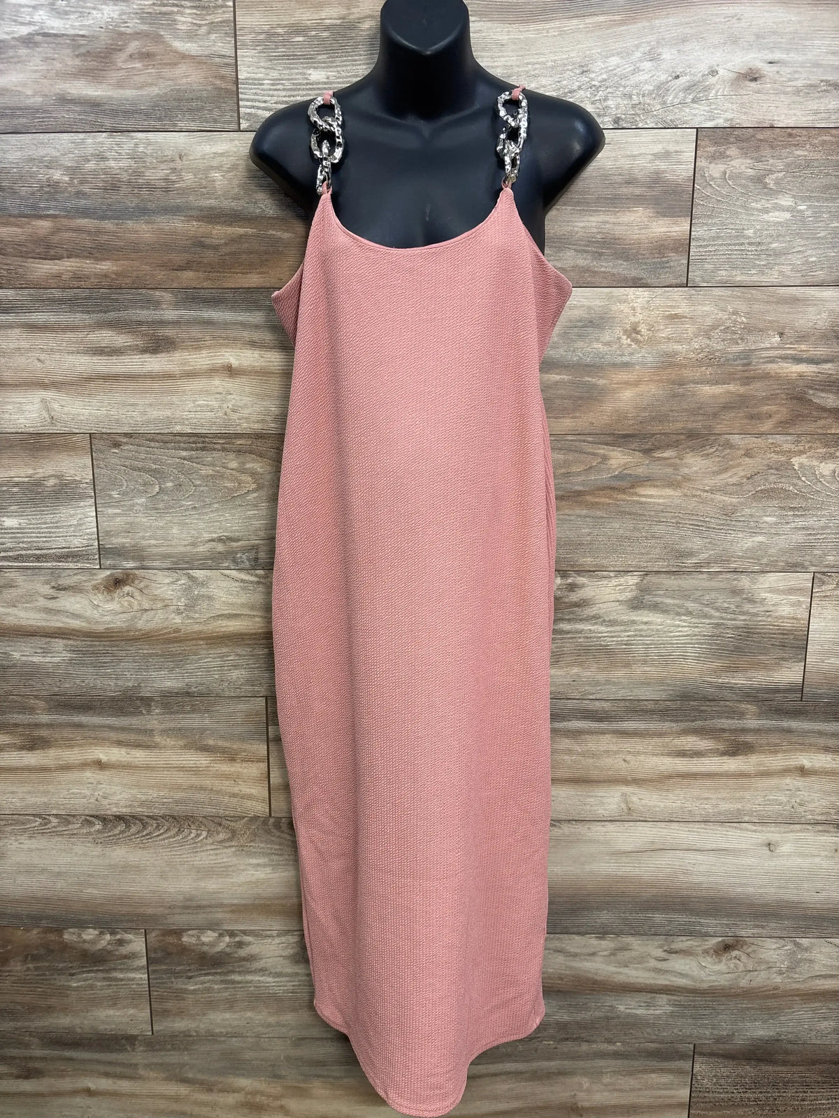 Pink textured sleeveless dress with chain straps on black mannequin against wood background