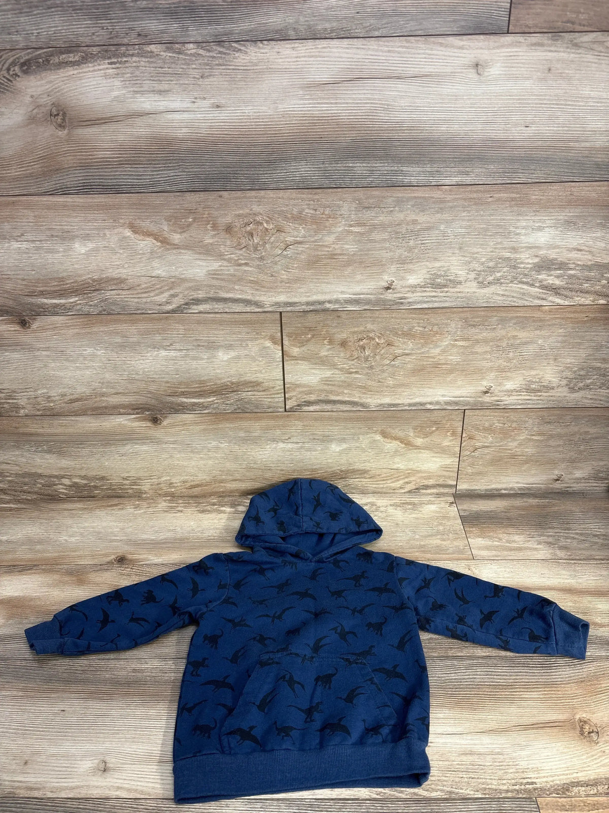 Navy blue kids hoodie with black dinosaur print laid flat on wood background