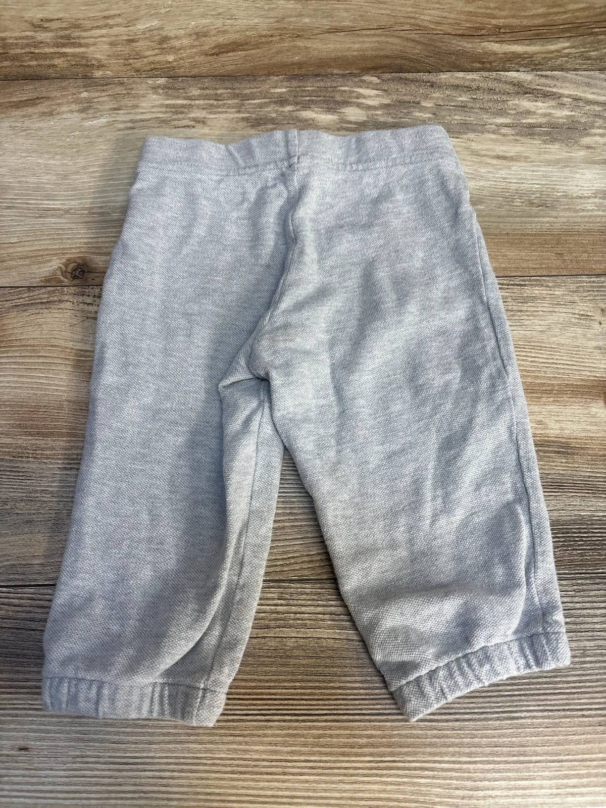 Front view of Ralph Lauren gray drawstring pants, size 12 months, with elastic waistband and cuffed ankles on wood