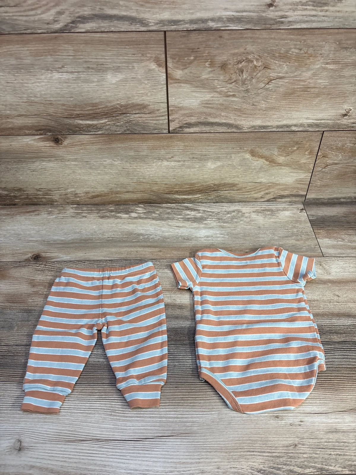 Flat lay of brown and white striped baby bodysuit and pants showing short sleeves and elastic waist on wood floor