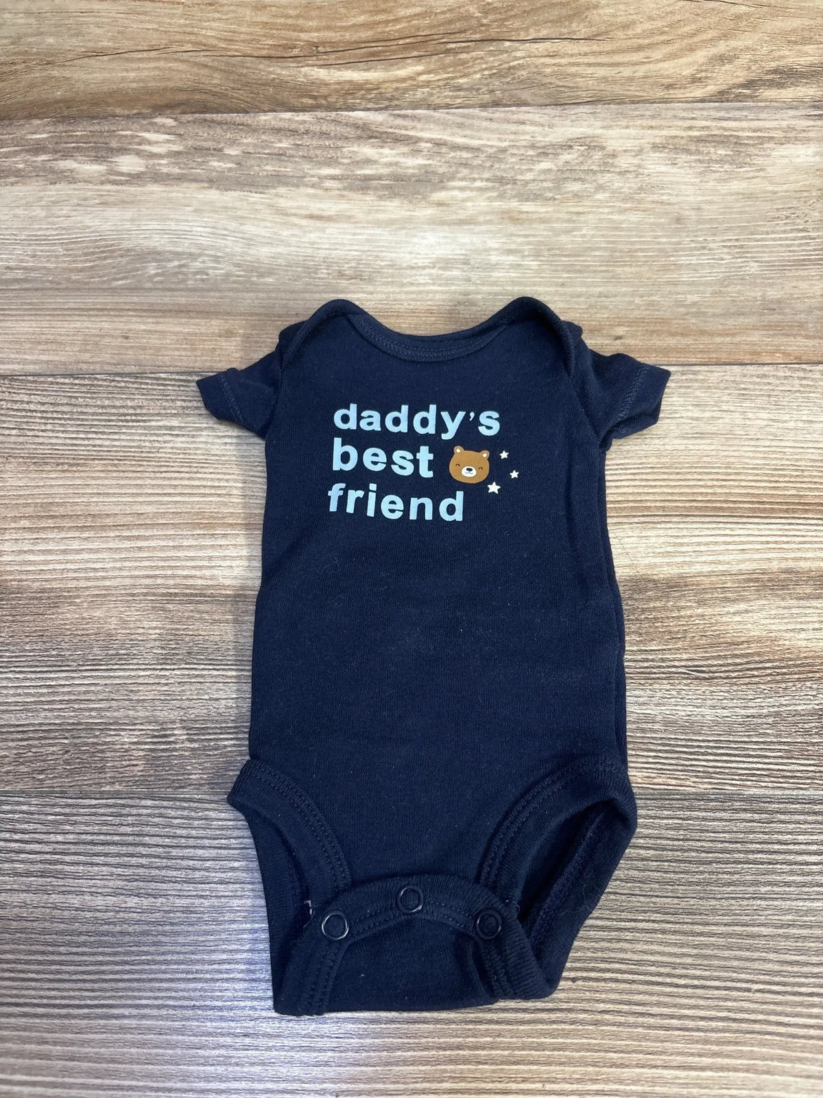 Top-down view of navy preemie bodysuit showcasing the text daddy's best friend with a small bear graphic on a wood background