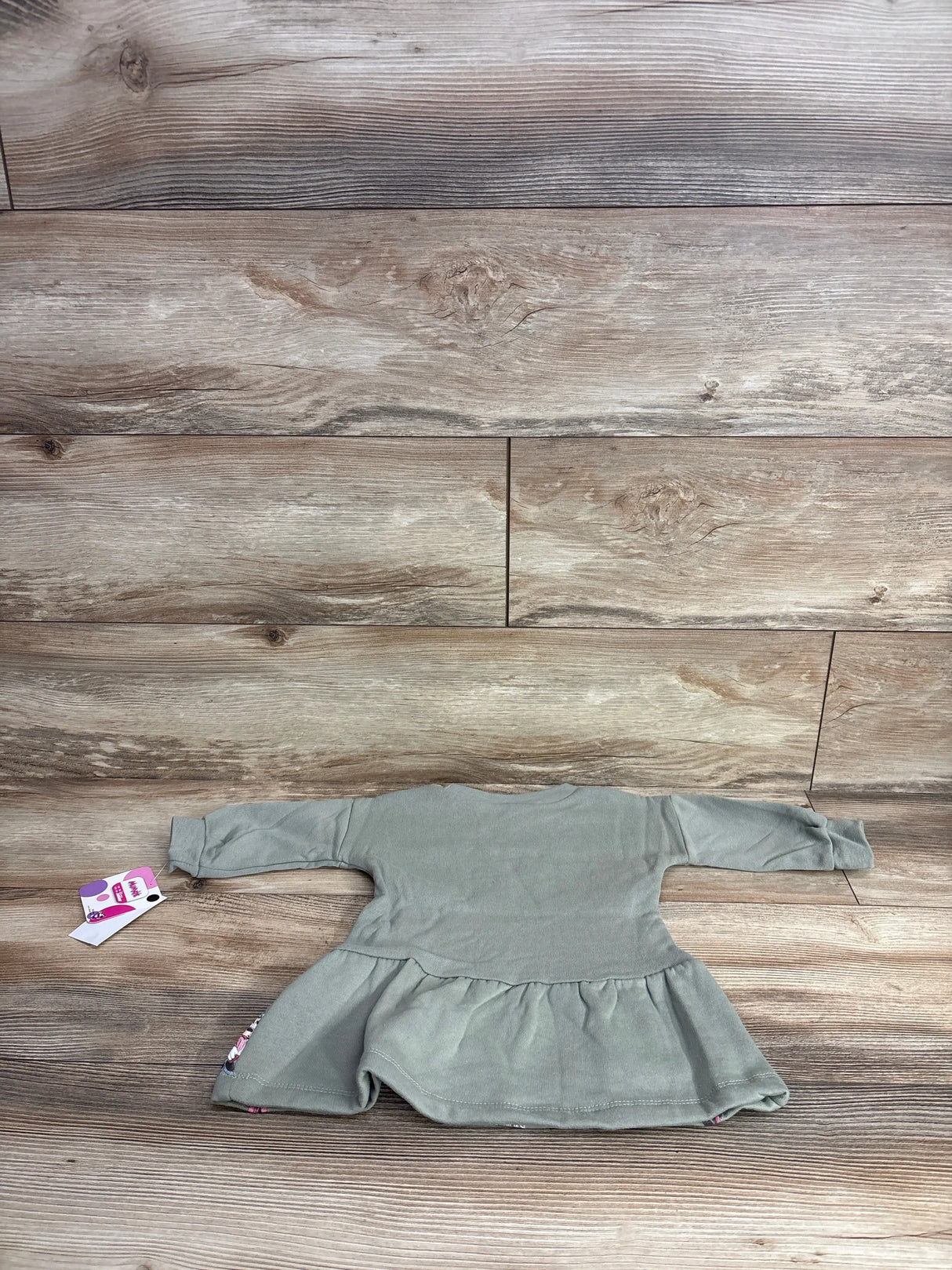 Long sleeve sage green baby dress with ruffle skirt, displayed on wood background