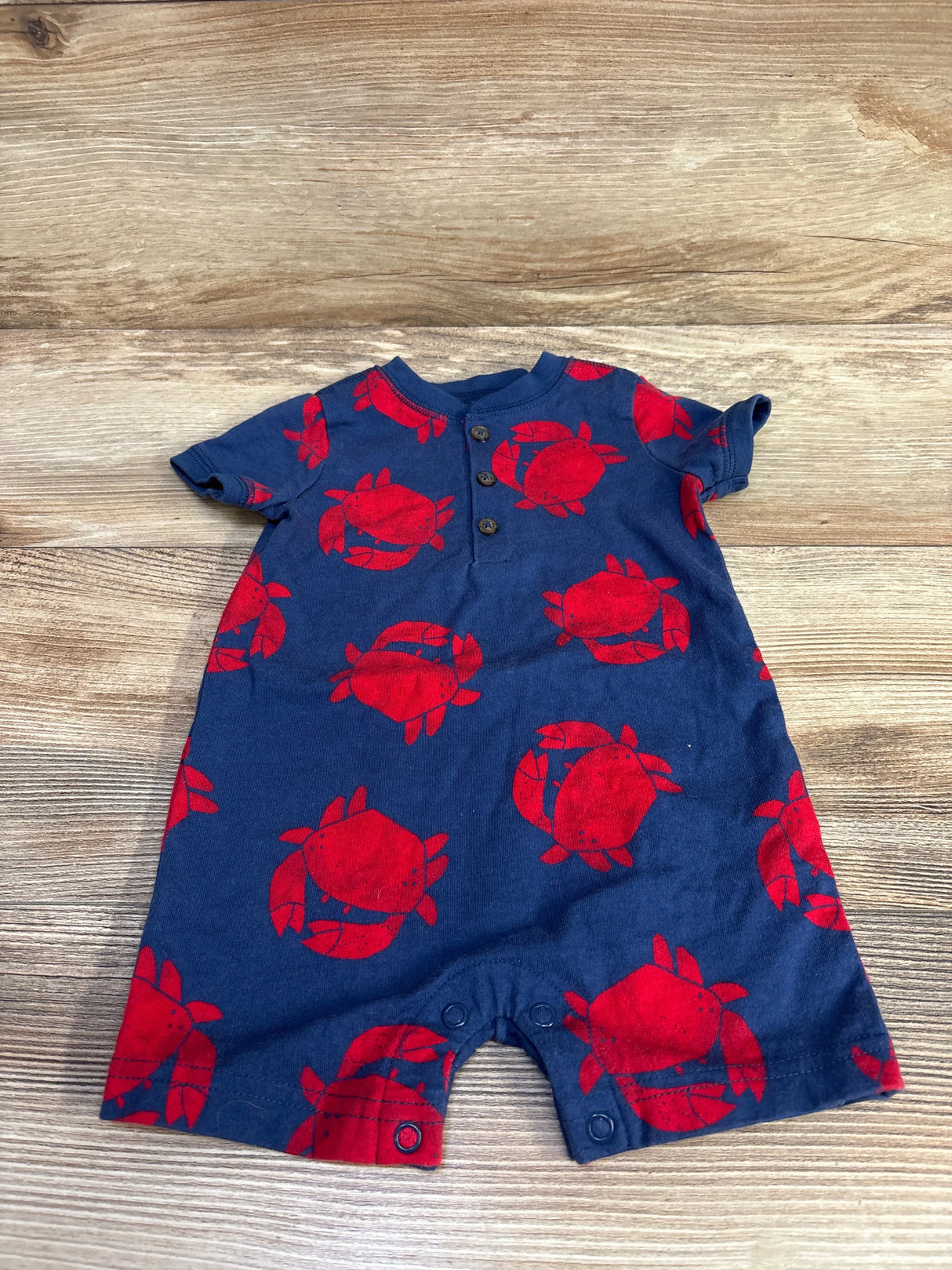 Navy blue baby romper with red crab print and buttons, laid on wooden surface