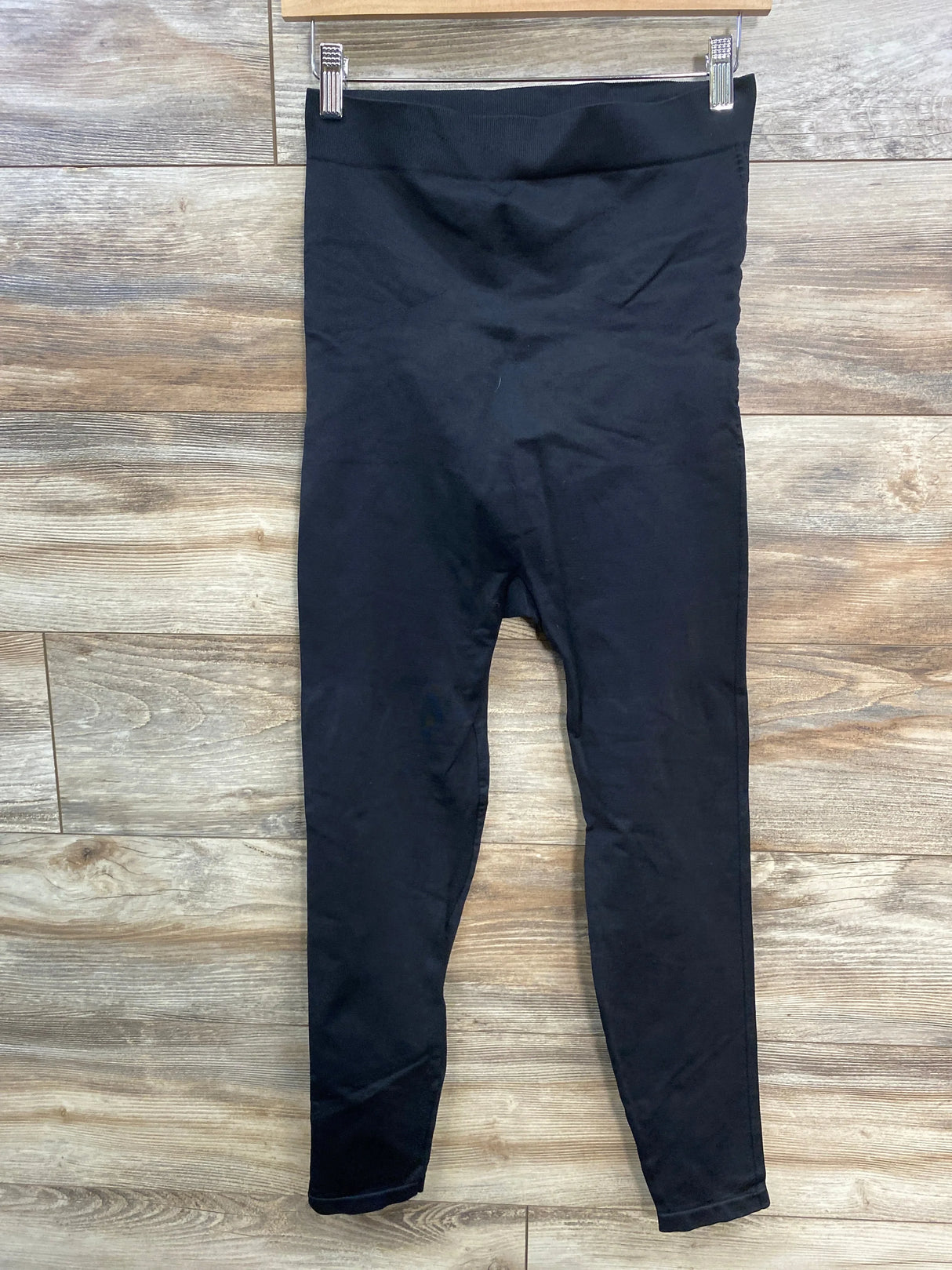 Black high-waisted leggings hanging on a wooden hanger against a wood background
