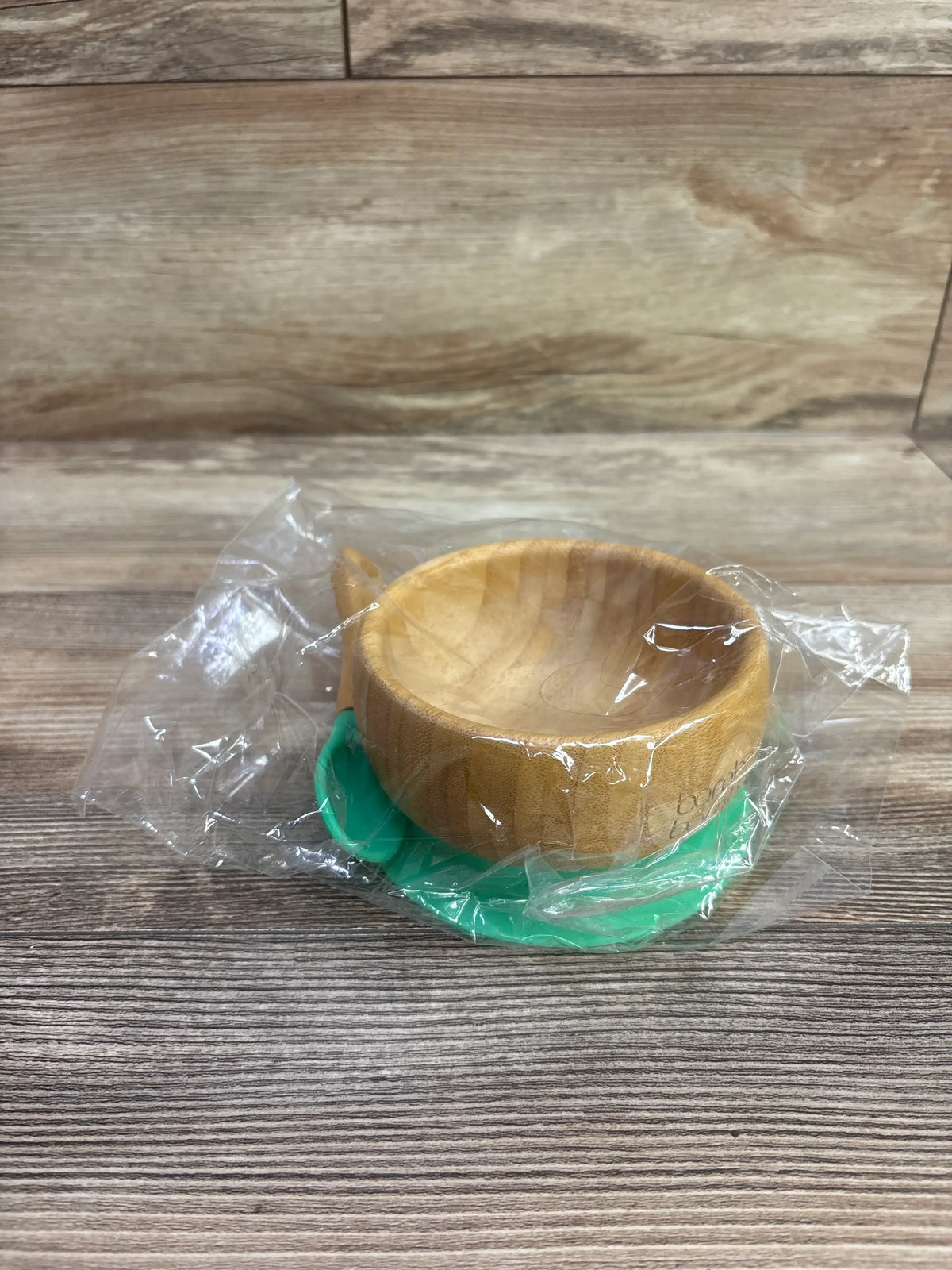 Front view of bamboo suction bowl and spoon set showcasing green suction base with wood-patterned background