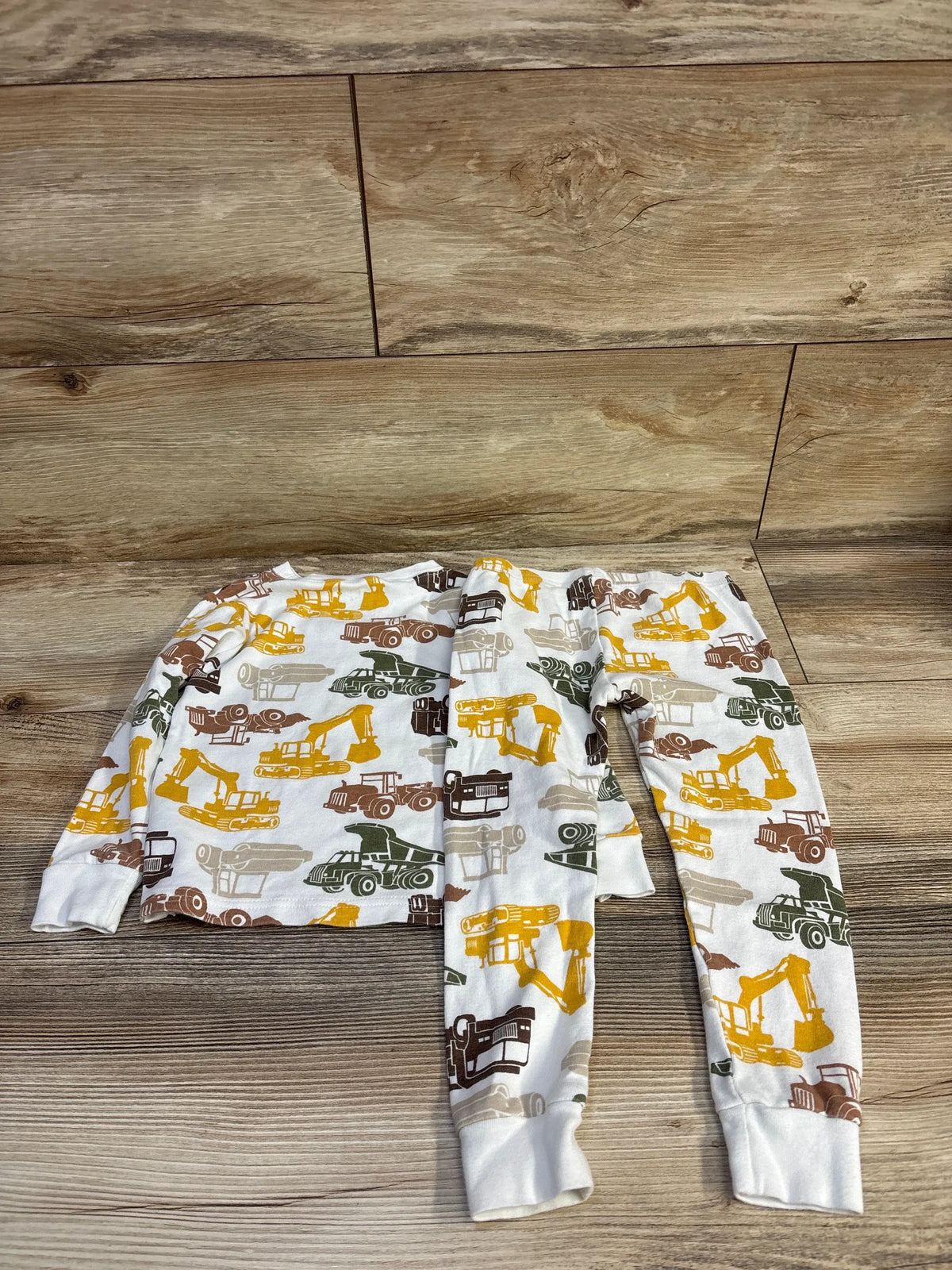 Top view of Carter’s white 2-piece toddler pajamas (3T) with multicolor construction-truck print, long sleeves and cuffed ankles on wood background