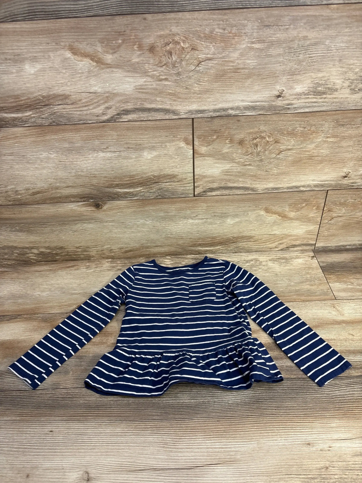 Navy blue and white striped long sleeve girls top with peplum hem on wood floor