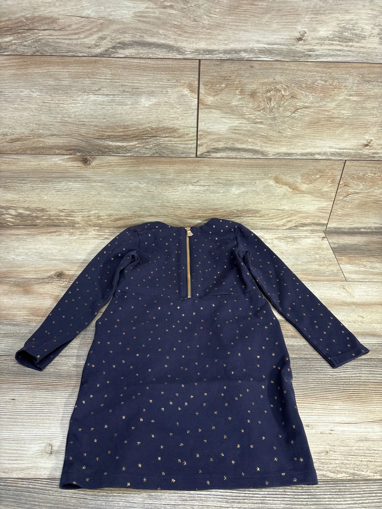 Navy blue long sleeve girls dress with gold star pattern and back zipper on wood floor