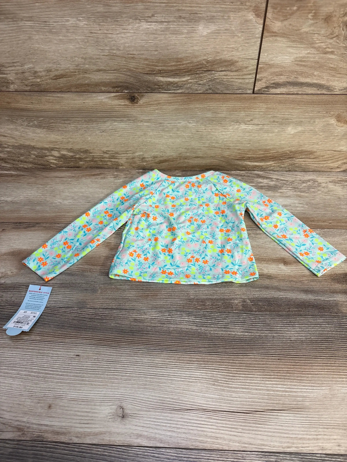 Flat lay of NEW Cat and Jack Floral Long Sleeve Rashguard Top Blue sz 2T showcasing pastel floral print with hangtag on wood plank floor