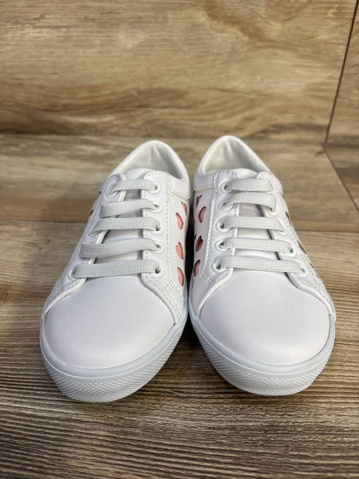 Front view of Janie & Jack heart sneakers showcasing white color, heart details, and bungee laces on a wood floor