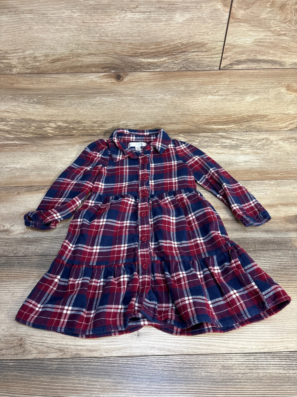 Red and navy plaid long sleeve girls dress with buttons, laid on wooden floor