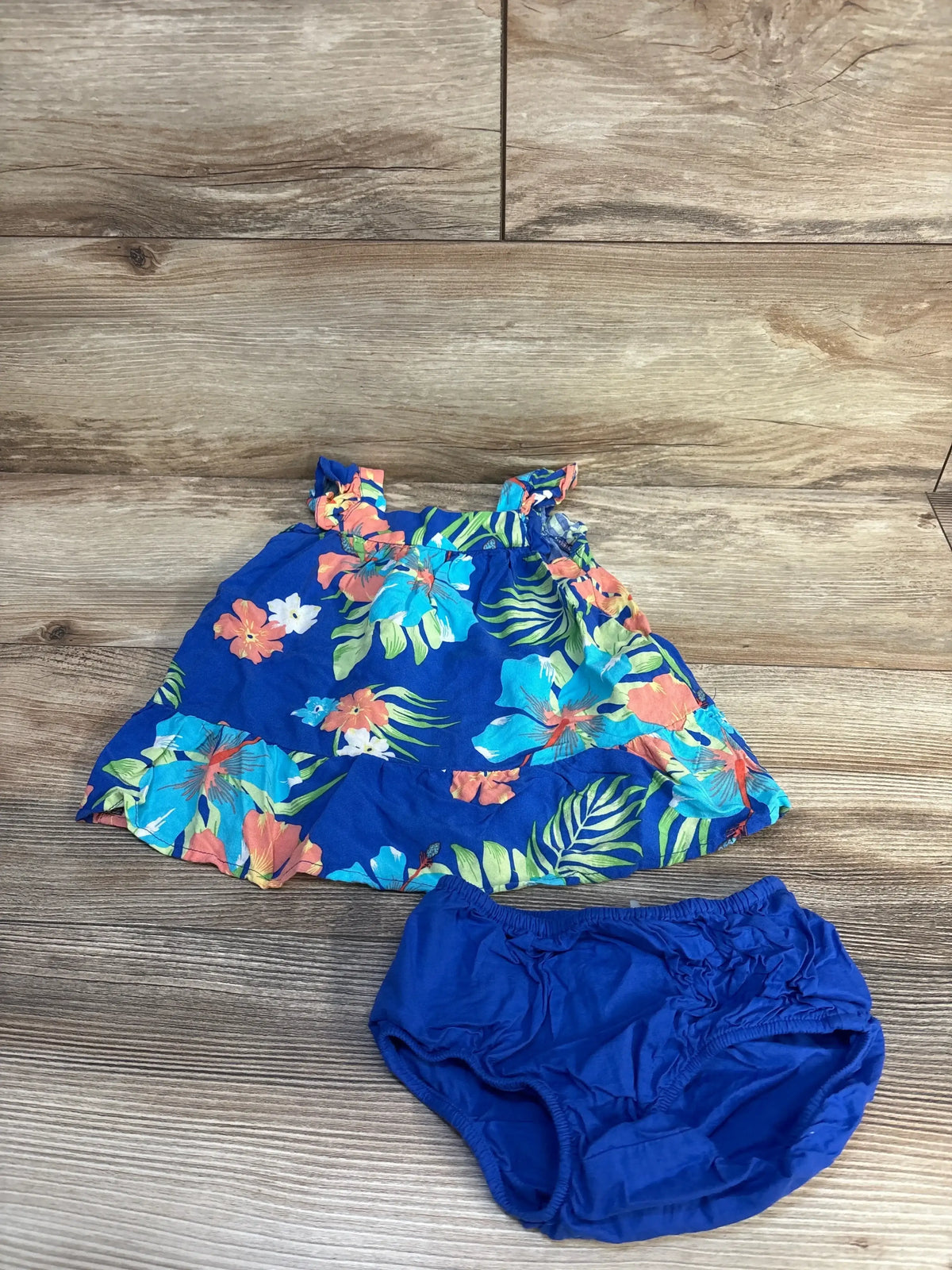 Flat lay of Children's Place 2-piece blue floral dress with matching blue bloomers showcasing tropical floral print and ruffle hem on a wood floor