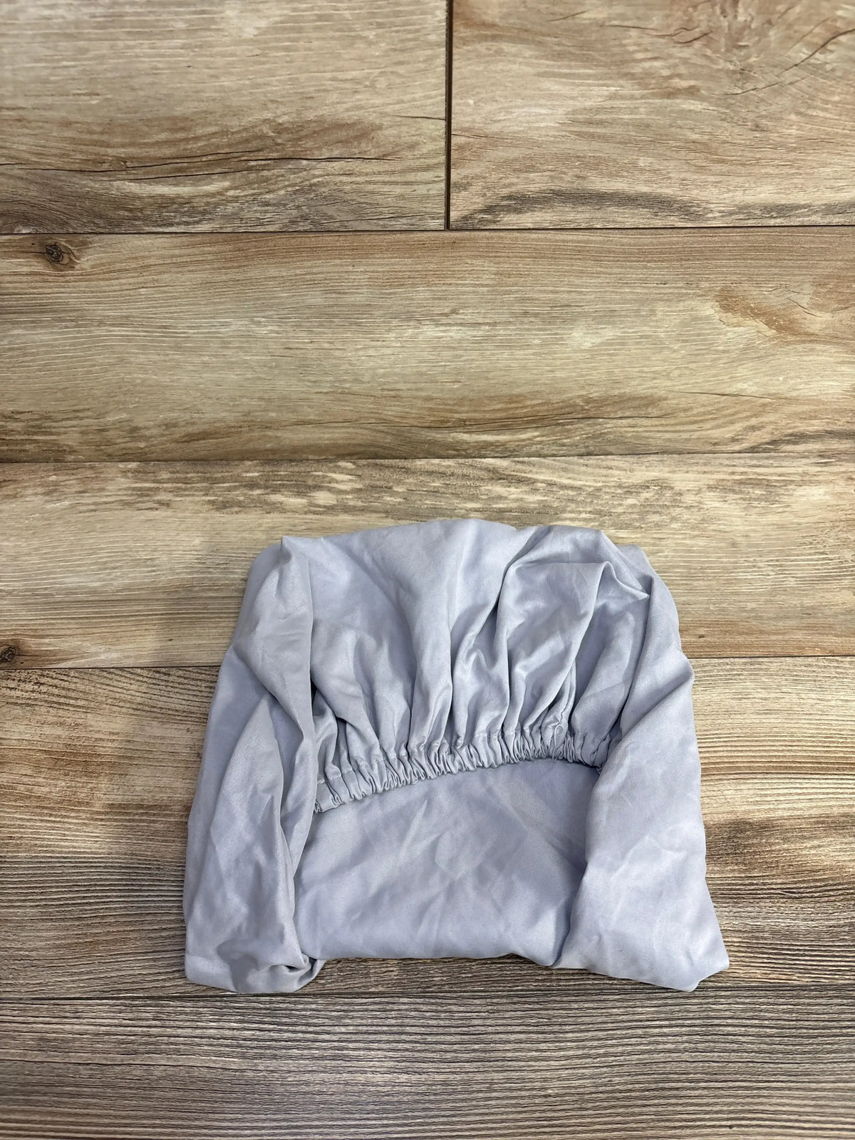 Light gray fitted sheet with elastic edges folded on wooden floor, kids bedding accessory
