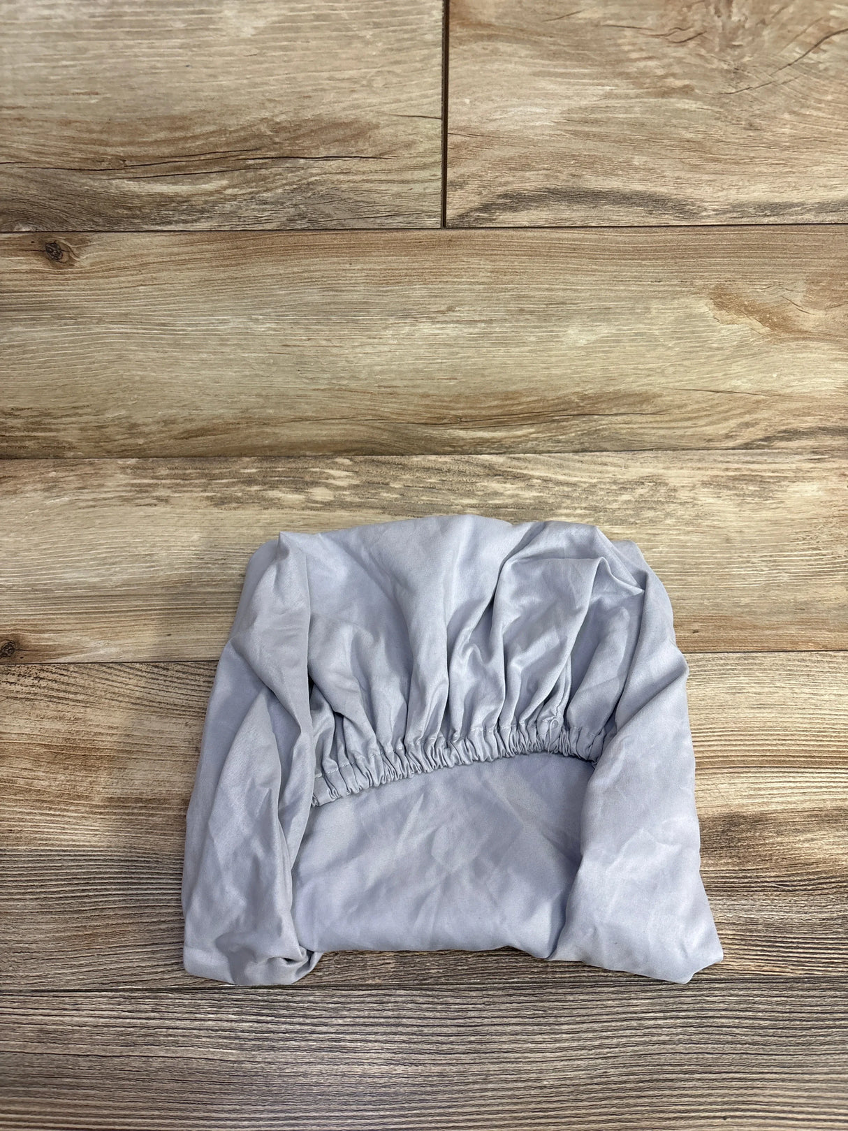 Light gray fitted sheet with elastic edges folded on wooden floor, kids bedding accessory