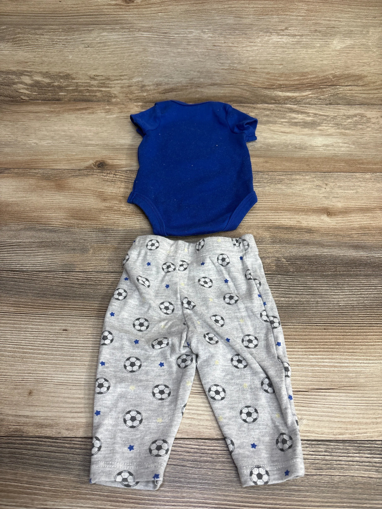 Blue baby bodysuit with gray soccer ball print pants set on wooden background