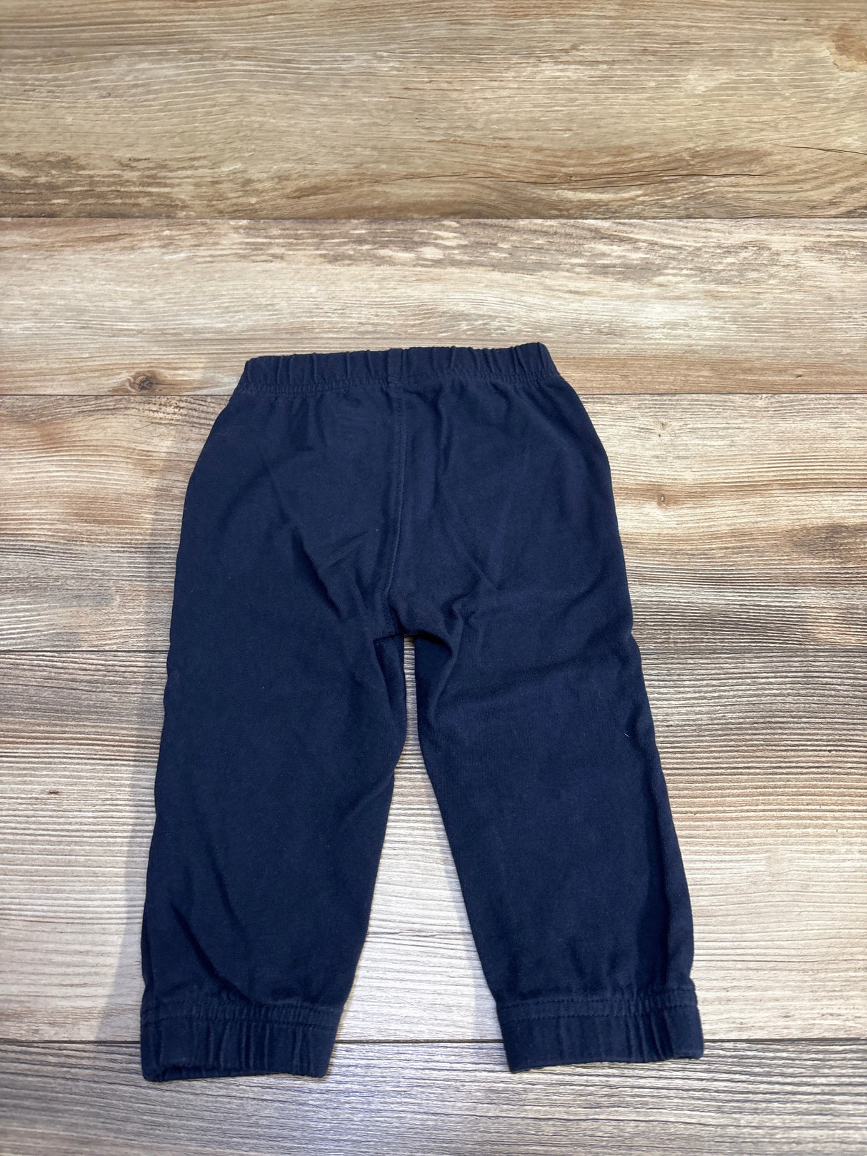 Front view of Baby Gap navy toddler joggers showing elastic drawstring waistband and gathered cuffs on wood background