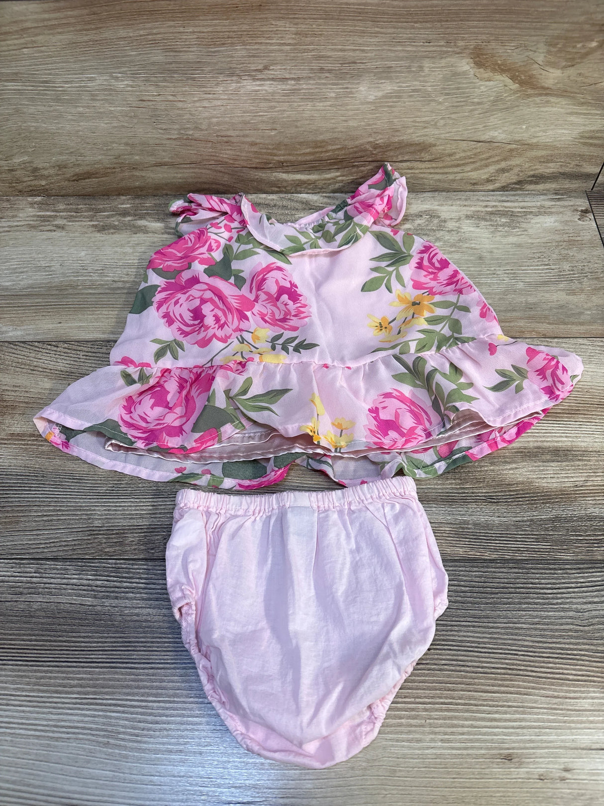 Pink floral baby dress with ruffle sleeves and matching diaper cover on wood floor