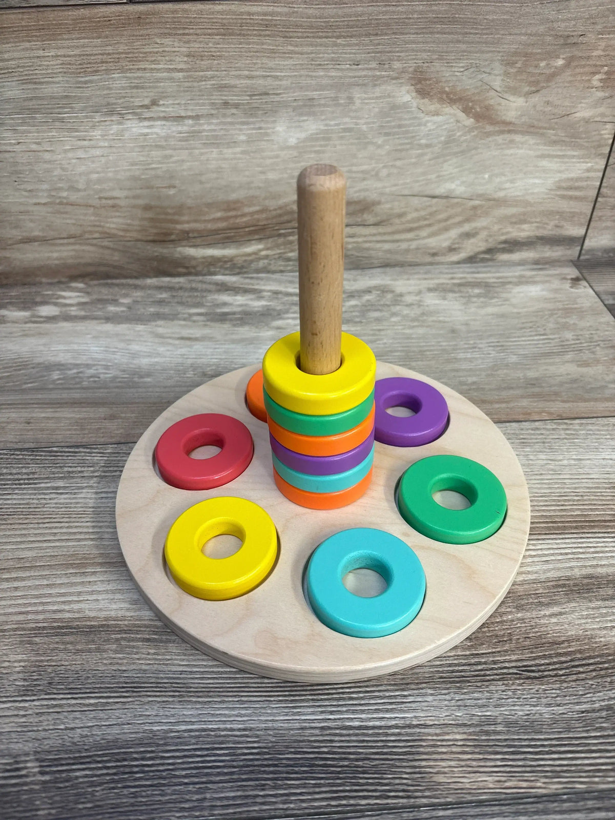 Front view of Lovevery Flexible Wooden Stacker with stacked colorful rings on central peg and natural wood base