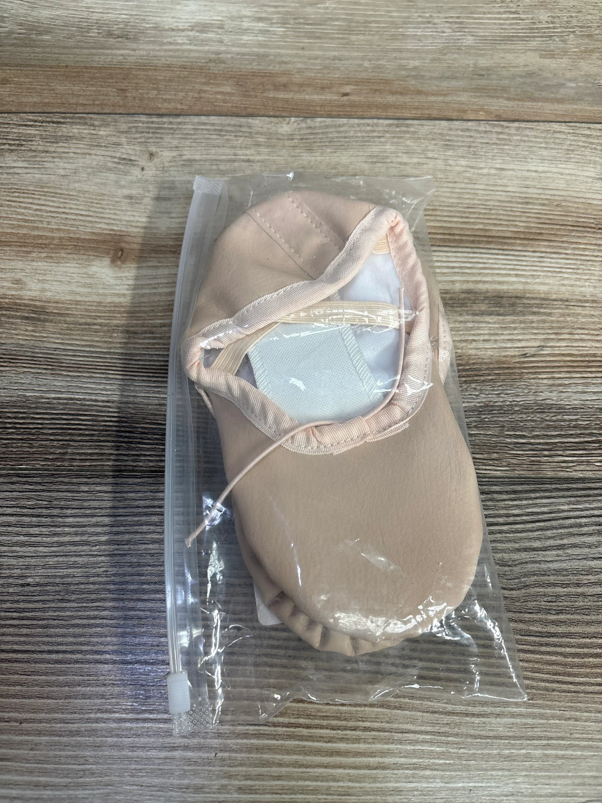 Beige baby ballet slipper in sealed plastic bag on wood background