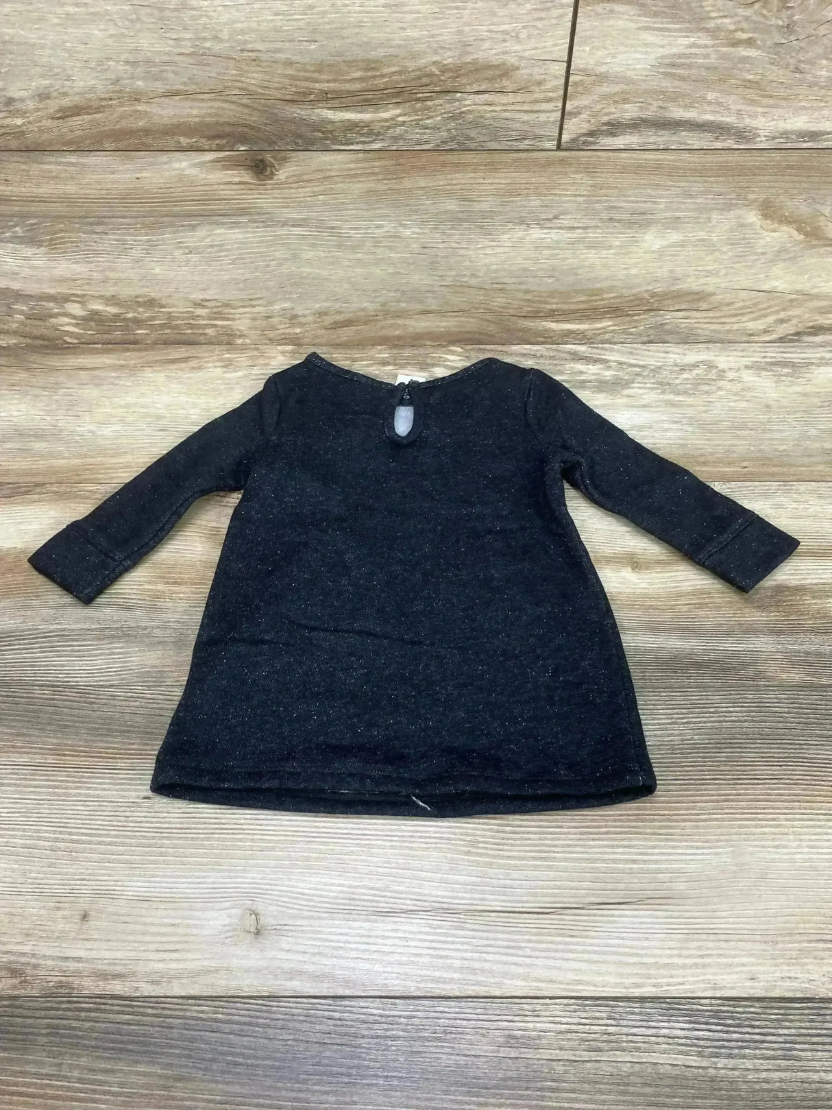 Flat lay of Old Navy black fleece shift dress showcasing long sleeves and back keyhole button on wood floor