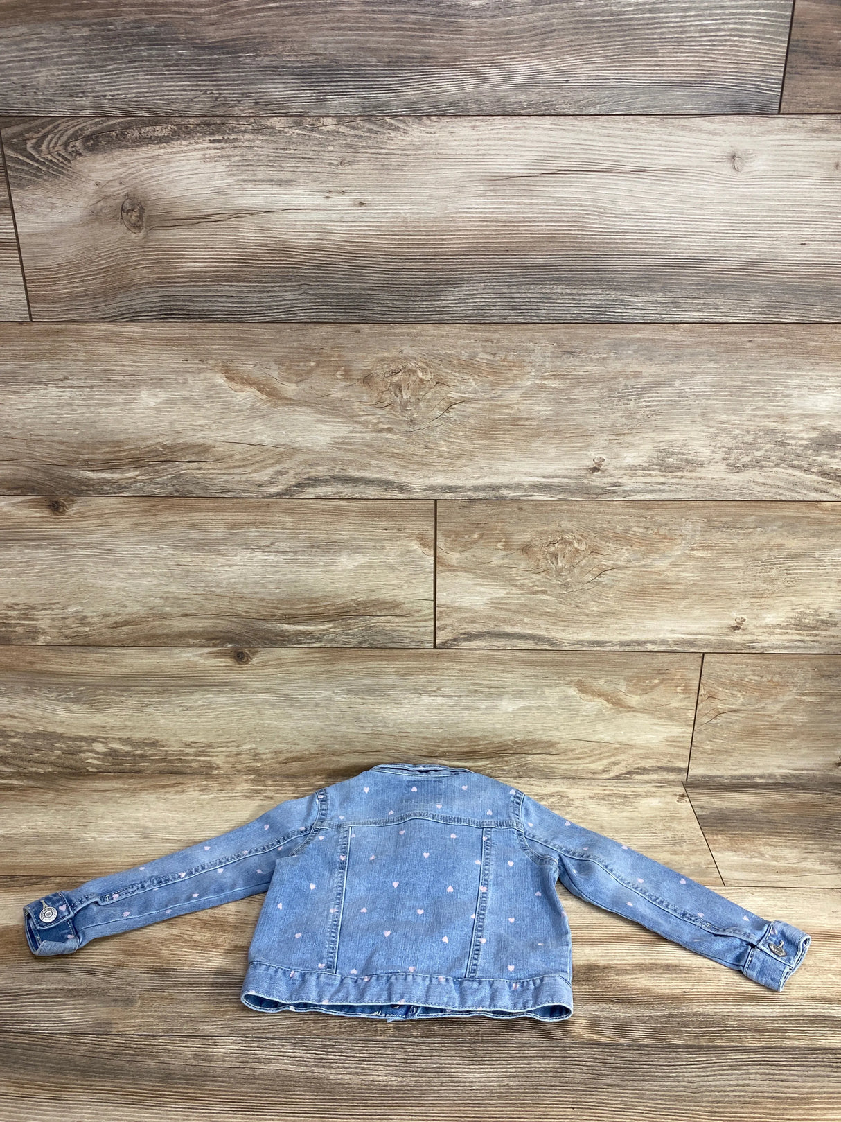 Light wash denim kids jacket with pink heart print detail on wooden floor background
