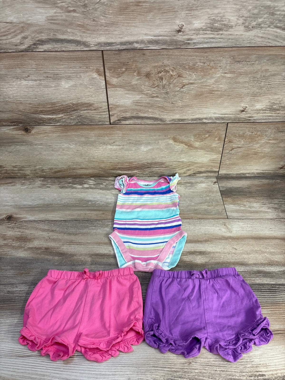 Front view of Children’s Place three-piece set showing striped bodysuit with pink and purple ruffled shorts on wood floor