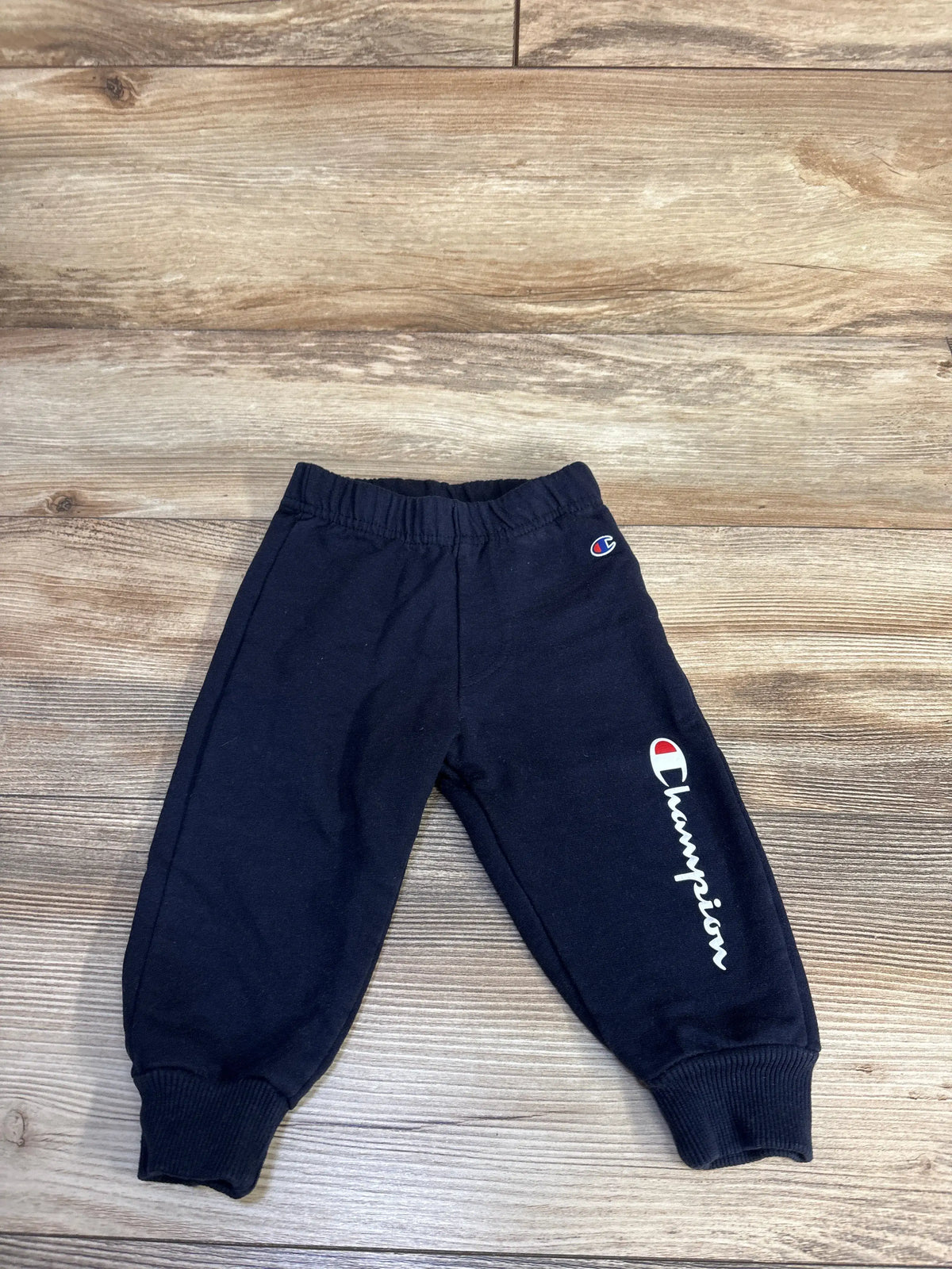 Front view of Champion navy joggers showcasing elastic waistband, tapered legs, and ribbed cuffs on a wood-grain background