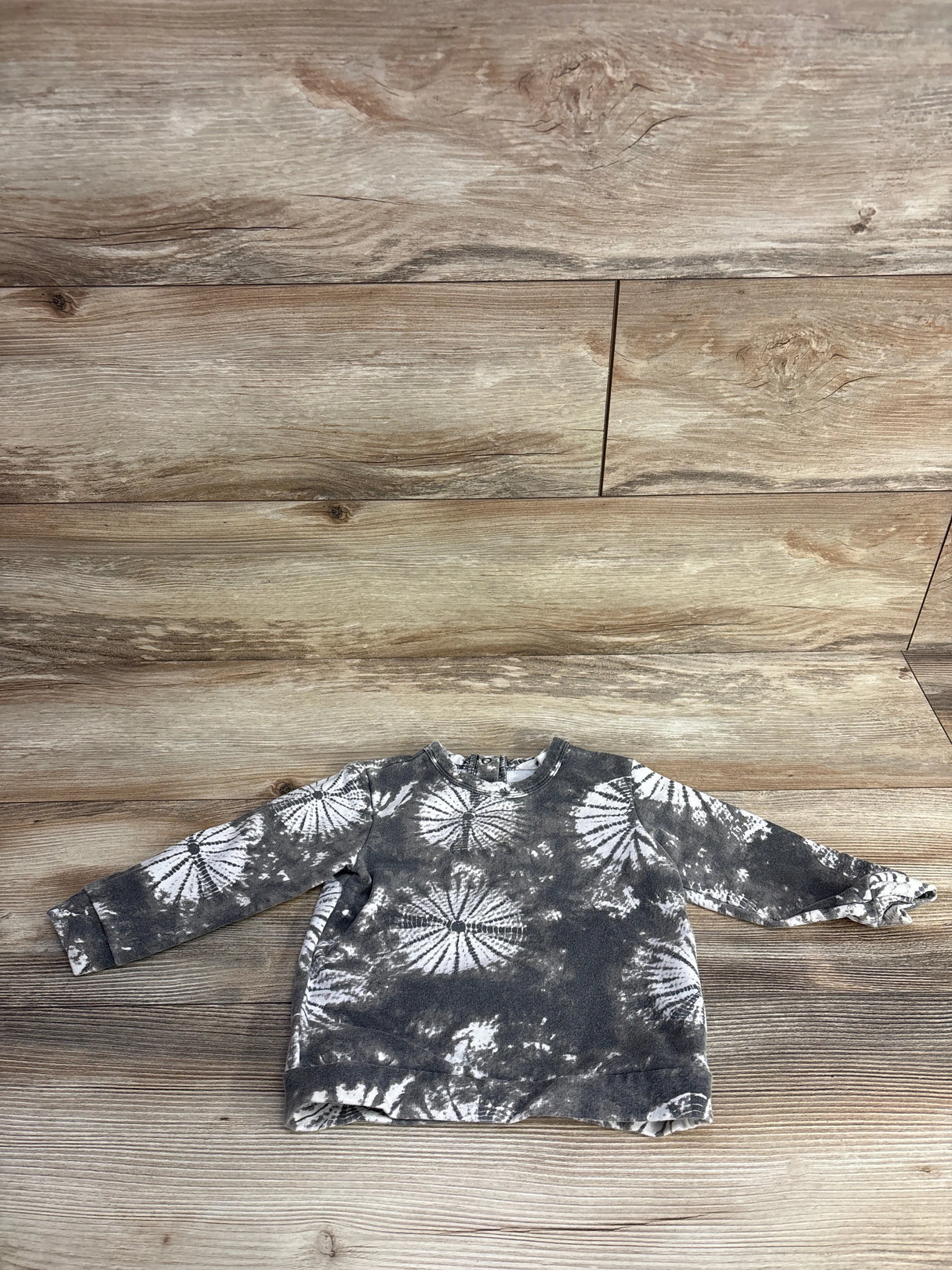 Child's long sleeve tie-dye sweatshirt laid flat on wood floor background