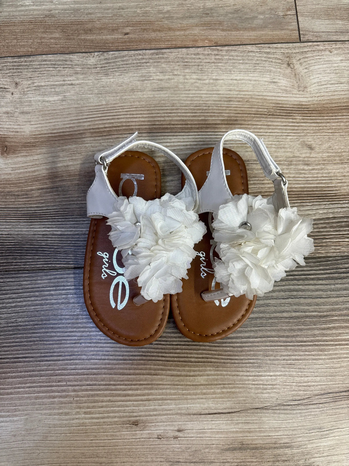 Top view of Bebe white chiffon flower sandals in size 7C showcasing large chiffon flower accents and ankle straps on a wood floor