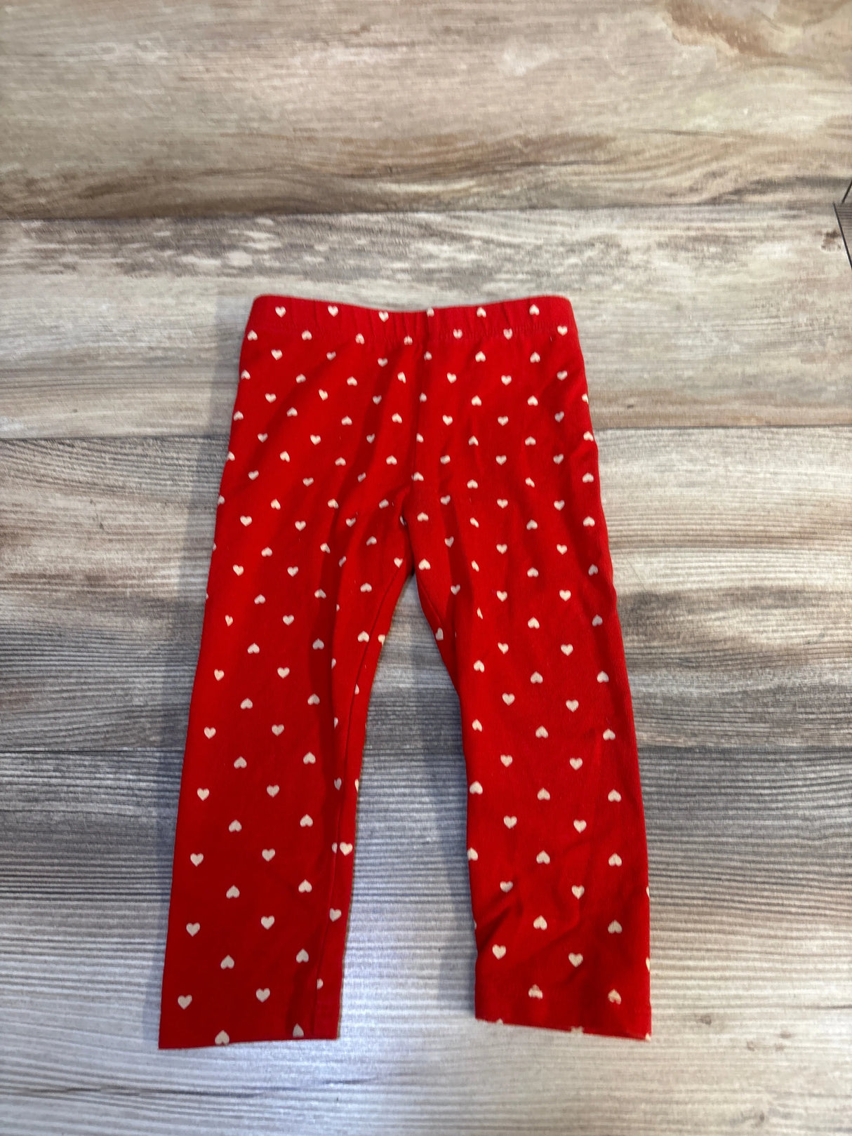 Red toddler leggings with white heart pattern on wooden background