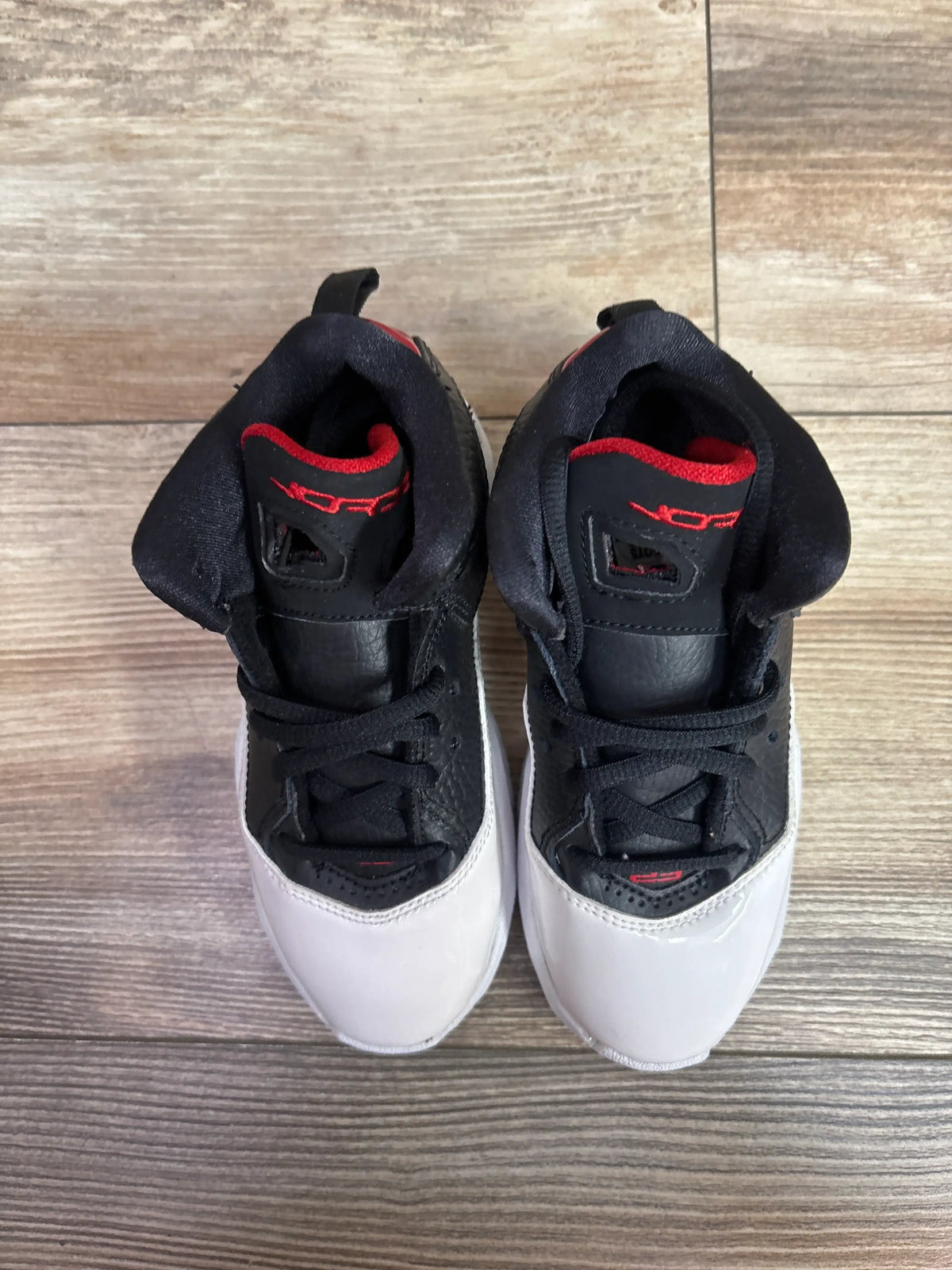 Top view of Air Jordan B’Loyal PS White Gym Red sneakers showcasing black uppers, red accents, and white toes on wood flooring