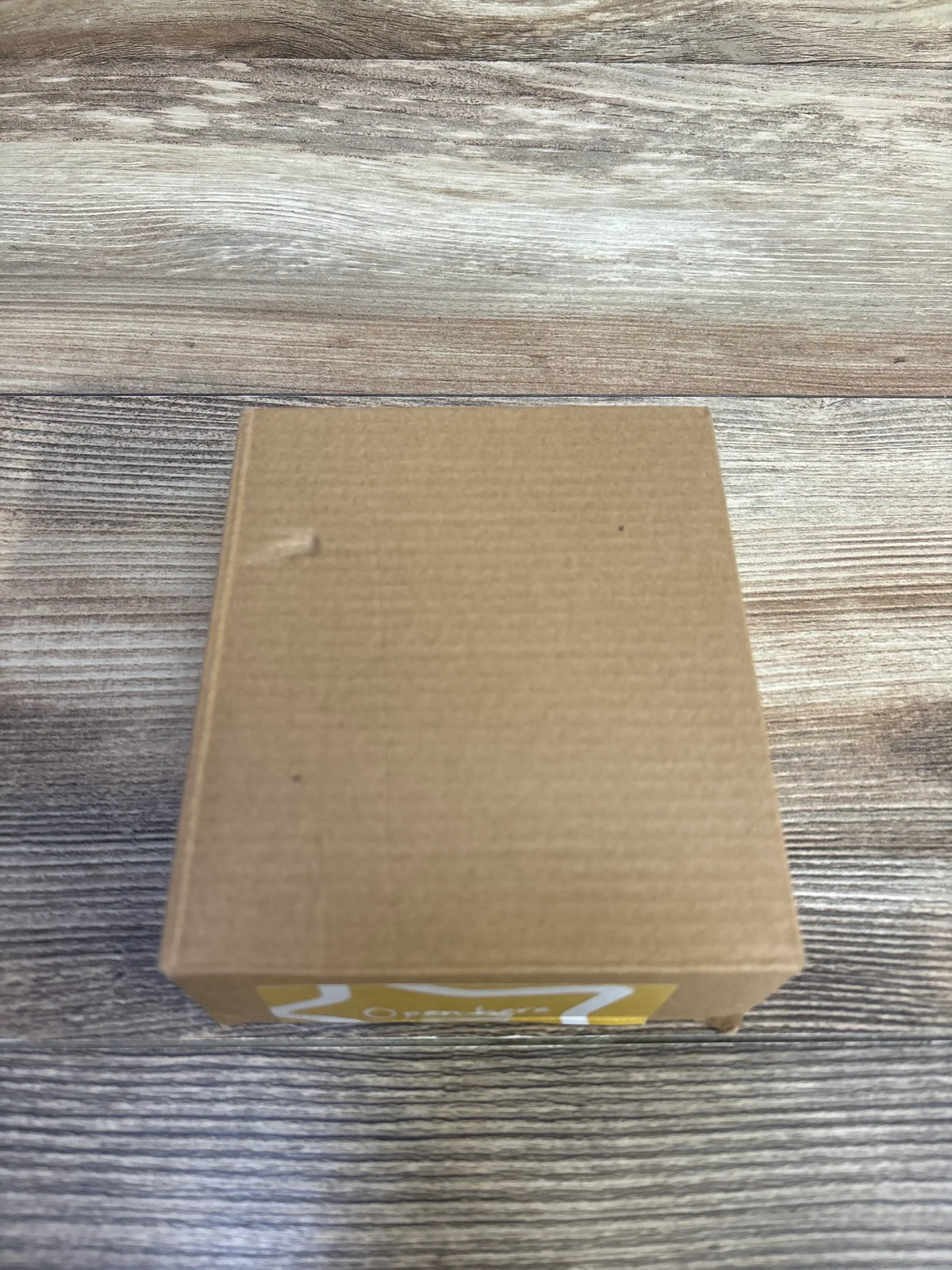 Top-down view of Tommee Tippee 4-pack soothers box, sealed brown cardboard with yellow sticker on wood background