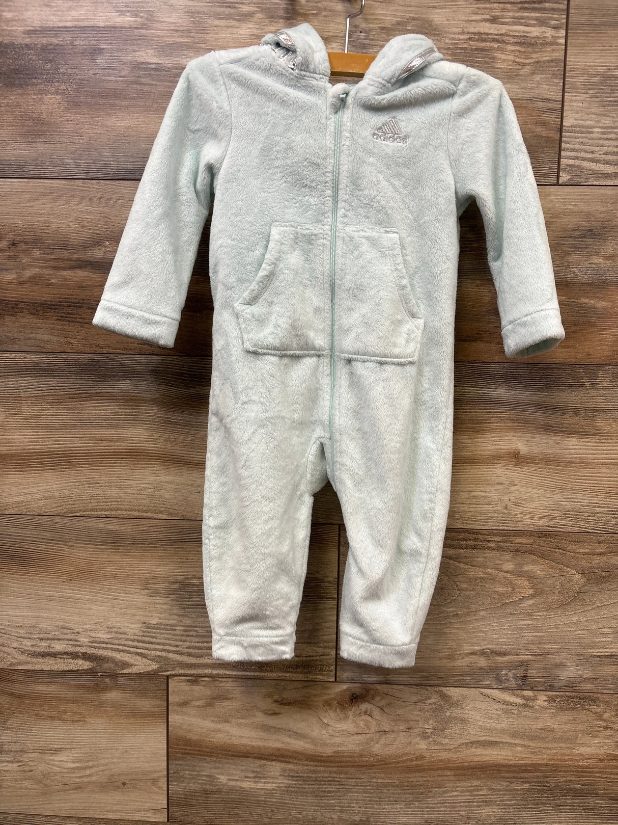 Light gray plush Adidas kids fleece jumpsuit with hood and front pockets on wooden background