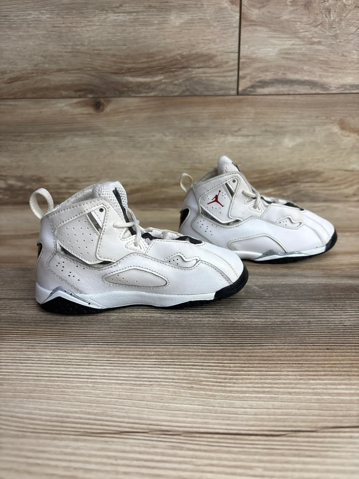 Angled view of Air Jordan True Flight GS sneakers in white size 10c showcasing red Jumpman logo and high-top on wood floor