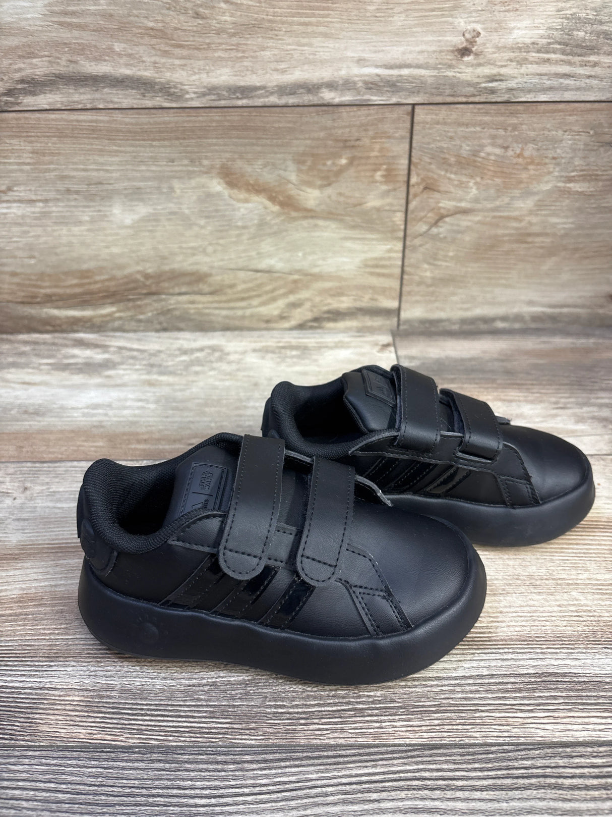 Three-quarter view of black Adidas x Star Wars toddler sneakers with double velcro straps and bubble sole on wood background
