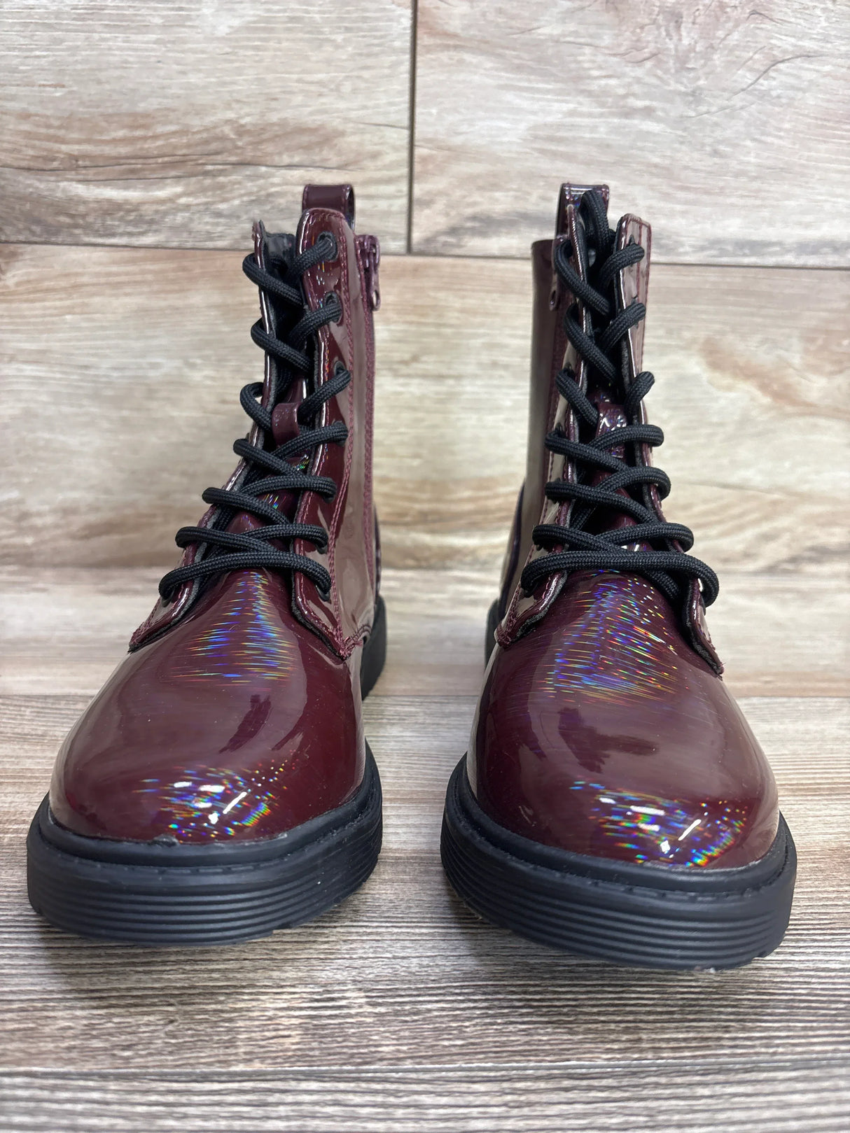 Burgundy patent leather kids combat boots with black laces on wood floor
