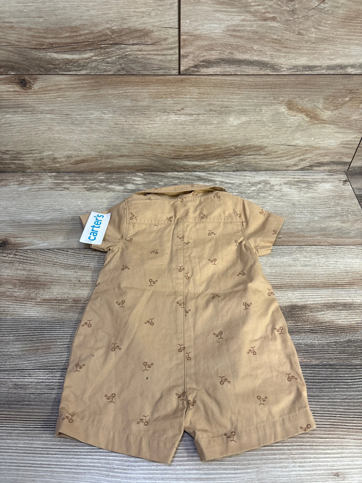 Front view of Carter’s tan polo romper in size 3 months, showcasing short sleeves and patterned fabric on a wood surface