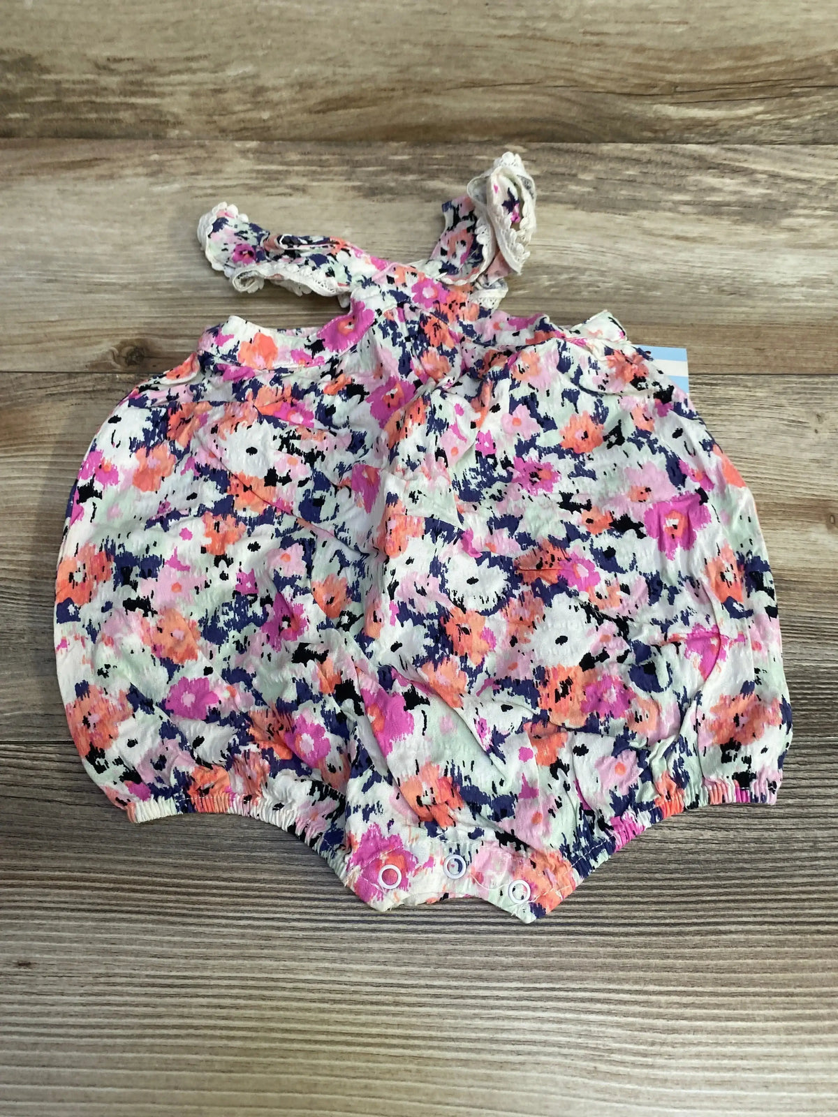 Top view of Cat & Jack newborn (0-3M) flutter-sleeve romper with pink floral print, lace straps and snap crotch on wood background