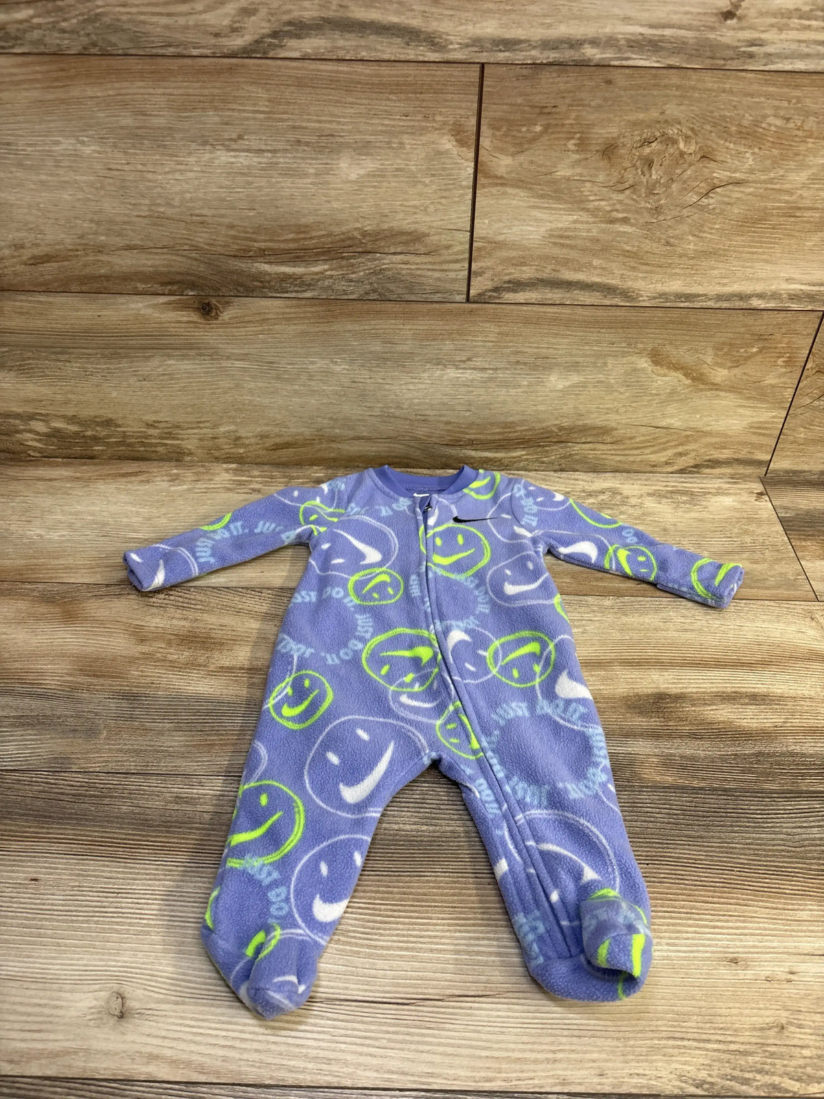 Flat lay of purple Nike footed blanket sleeper showing front zipper and green smiley swoosh print on wood surface, size 3 months