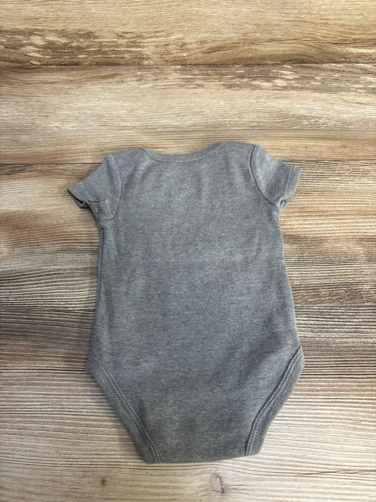 Flat-lay of grey Nike baby bodysuit, size 6M, showing short sleeves, crew neck, and snap crotch on wood background