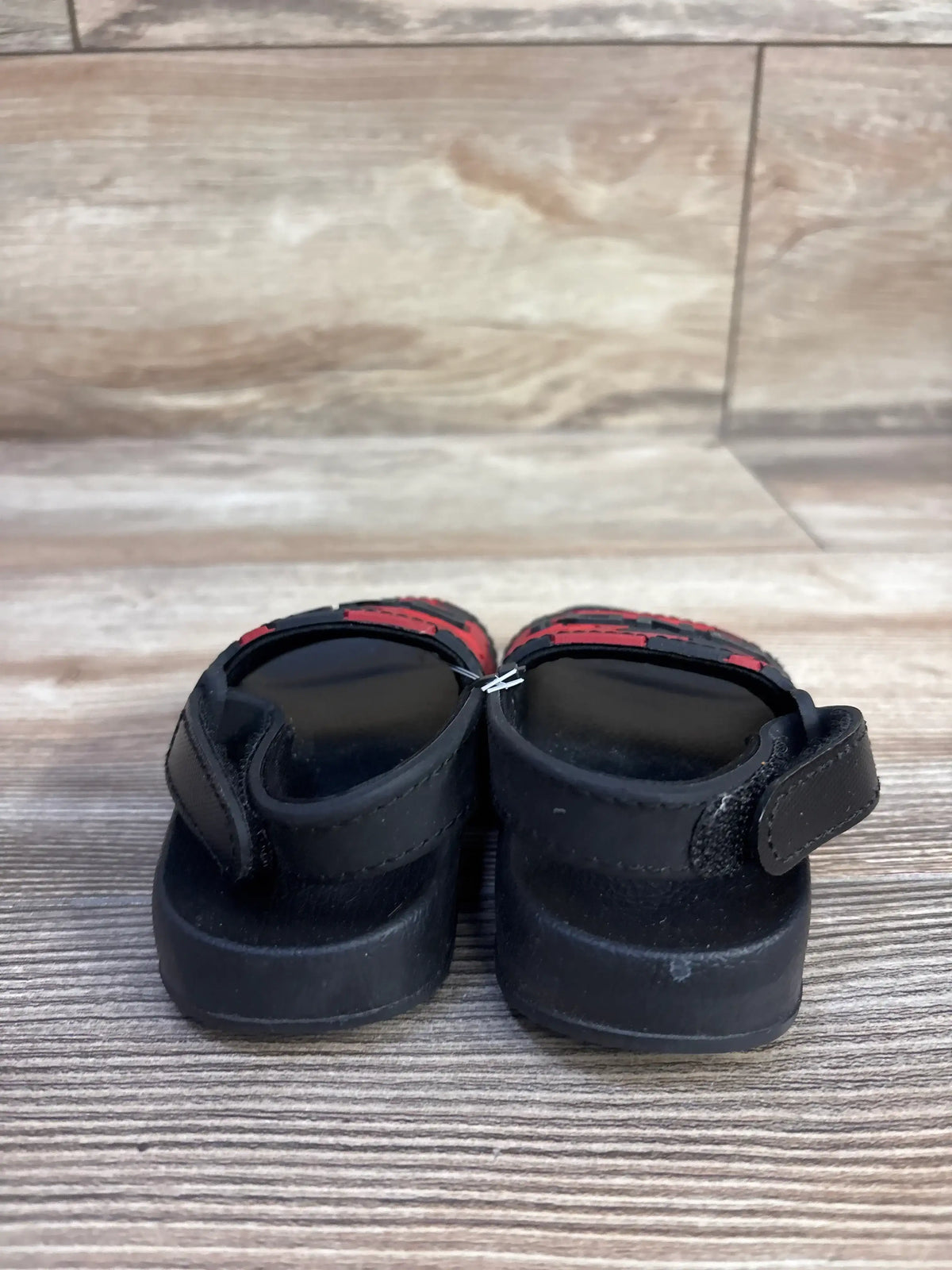 Rear view of And1 camo slide sandals in red and black showcasing hook and loop straps on a wood plank floor