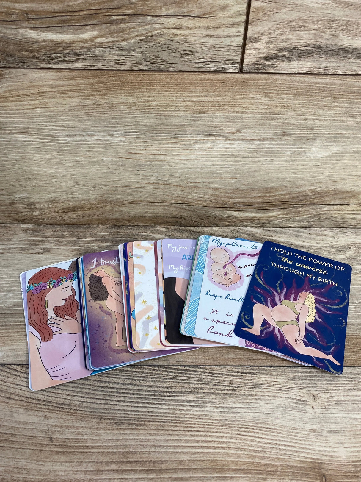 Fanned Pregnancy and Birth affirmation cards on wood showing headline 'I hold the power of the universe through my birth'