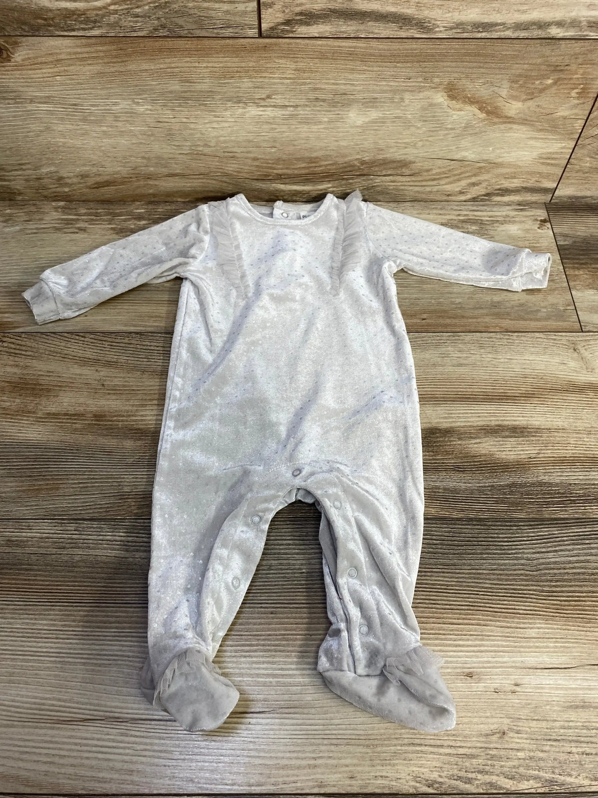 Light gray long-sleeve baby footed onesie with ruffle details on wooden floor