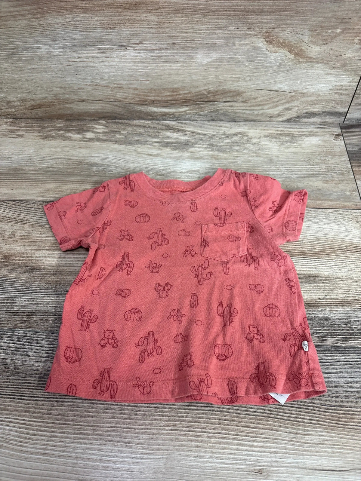 Front view of Baby Gap red cactus print pocket shirt with short sleeves and chest patch pocket on a wood-grain background