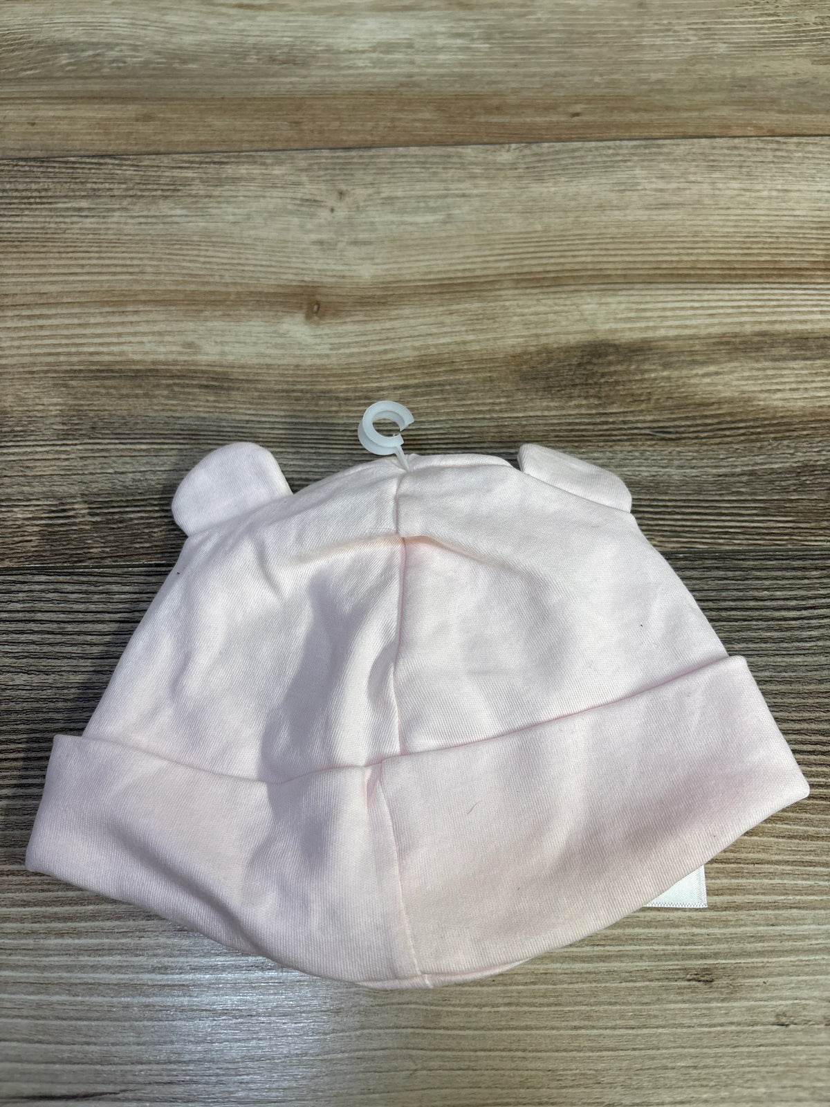 Top-down view of pale pink cotton baby beanie showcasing rolled cuff and small ear details on a wood tabletop