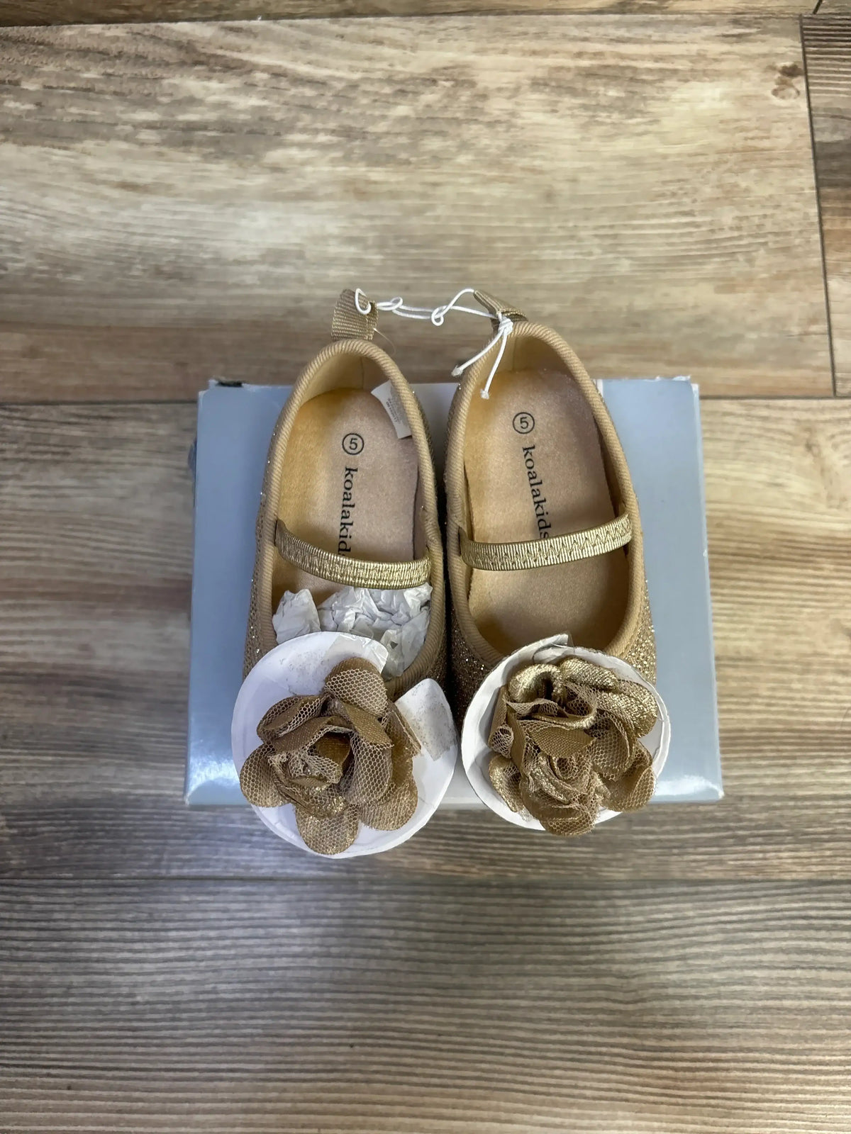 Top-down view of Koala Kids gold sparkle Mary Jane flats with elastic strap, floral embellishments, visible size 5 on blue box